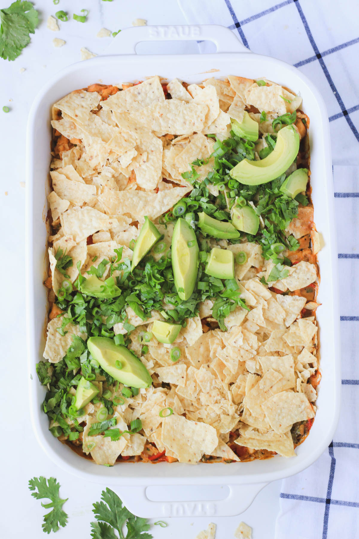 A white staub baking pan with dking ranch chicken casserole after baking on a white counter with a blue and white dish towel to the right.