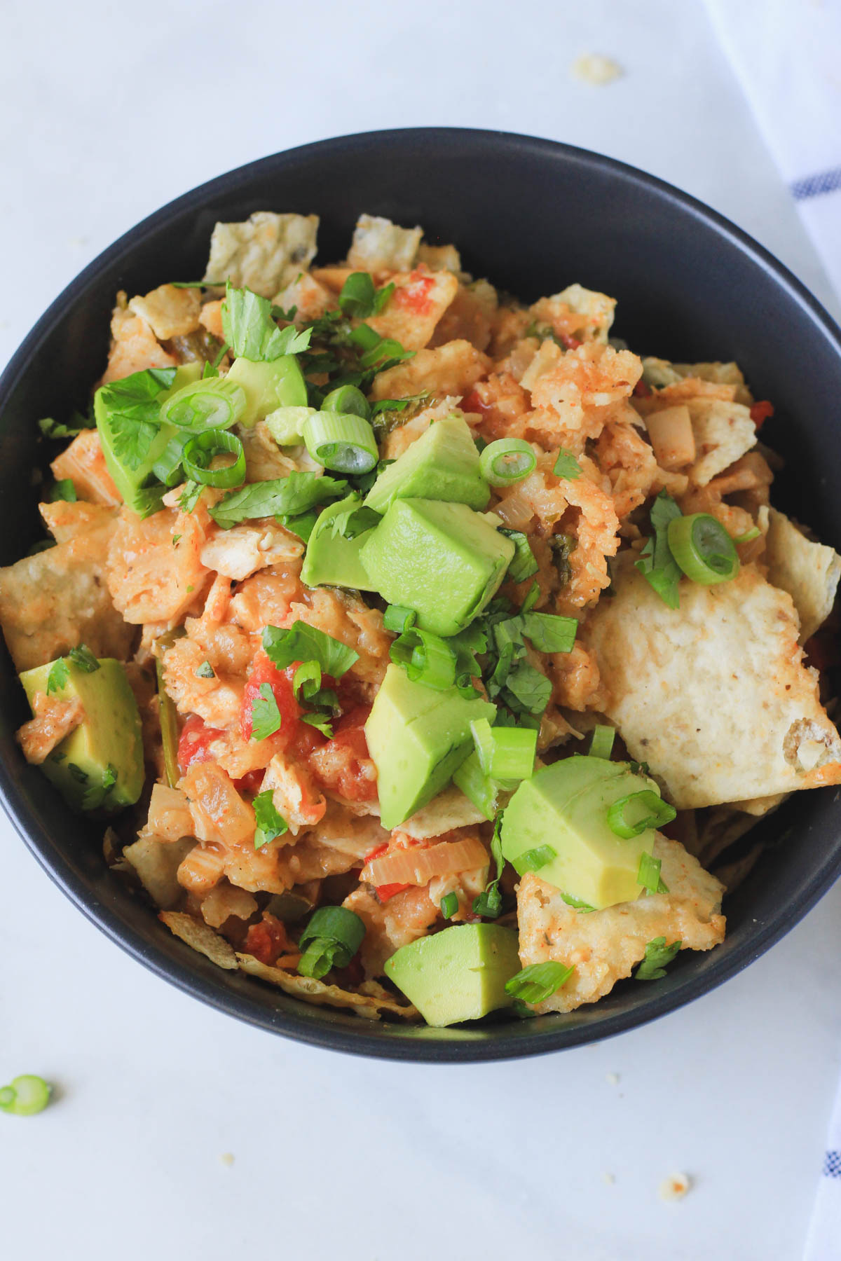 A dark blue bowl filled with king ranch casserole and topped with diced avocado, cilantro, and green onion.