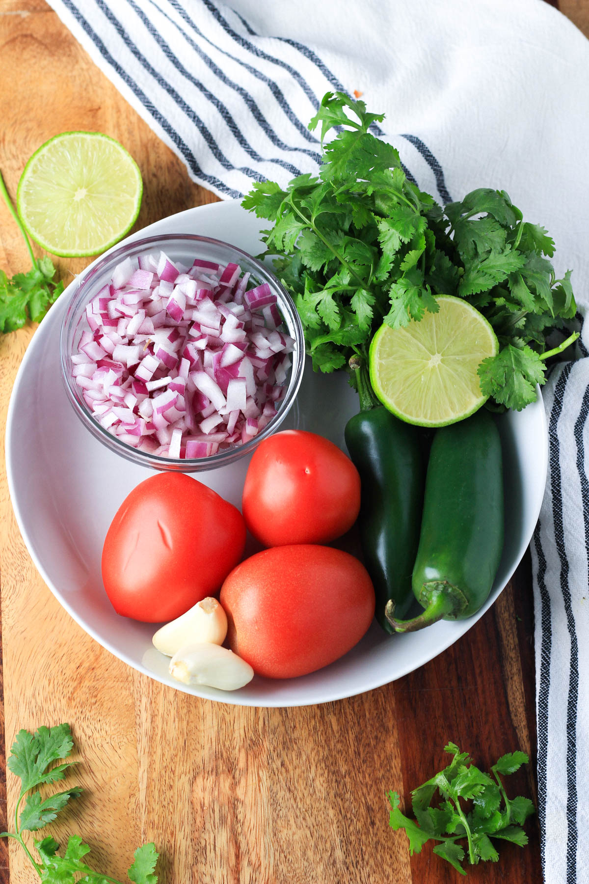 Ingredients for fresh pico de gallo in a white bowl on a wooden counter.