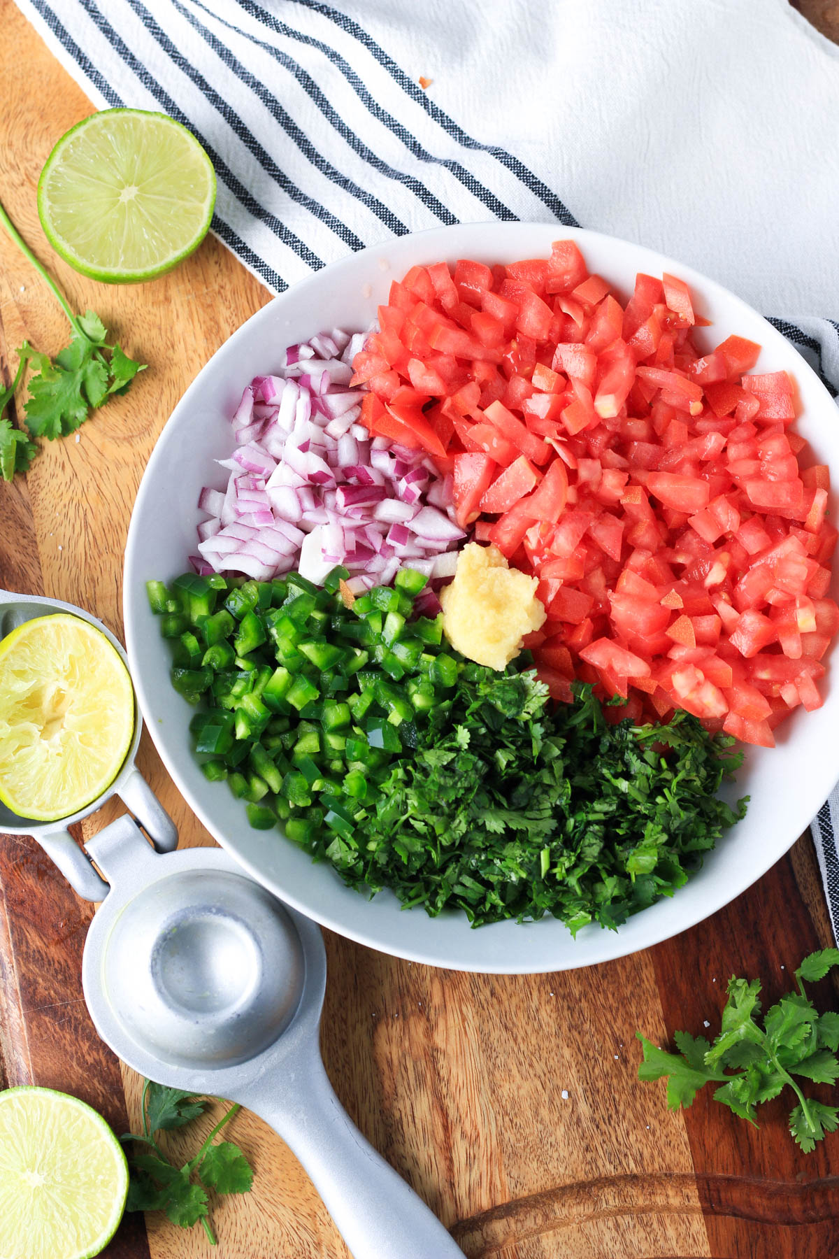 Diced vegetables in a white bowl with garlic in the middle and a lime juicer to the left.