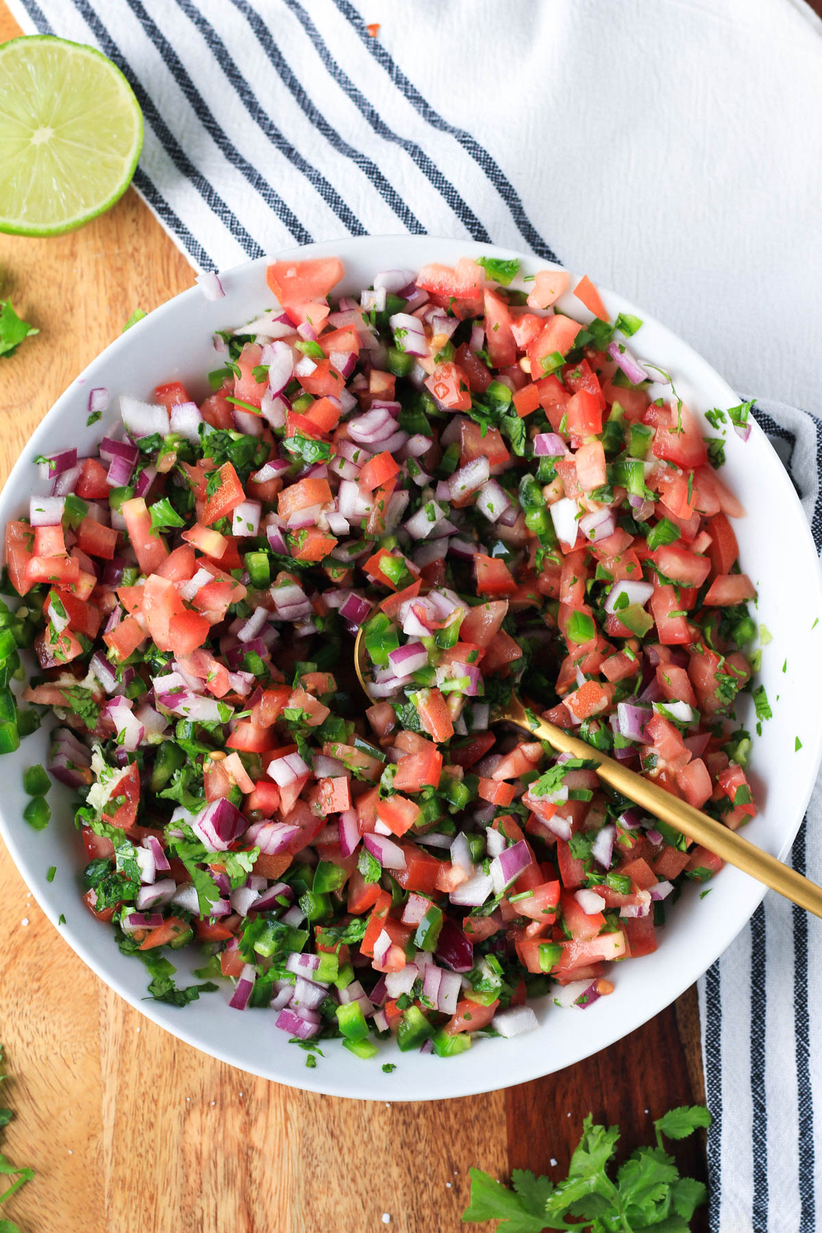 A white bowl with fresh pico de gallo after being mixed with a gold spoon.