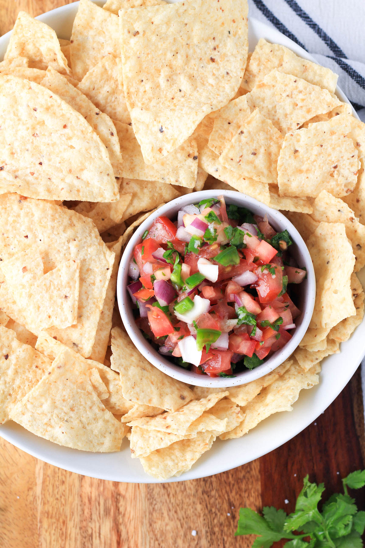 A white bowl with tortilla chips and a small bowl of pico de gallo in the bottom right of the white bowl.