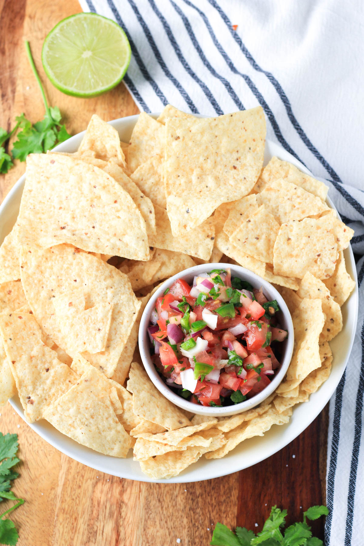 A large white bowl of tortilla chips with a small white bowl of vegan pico de gallo in the bottom right of the bowl.