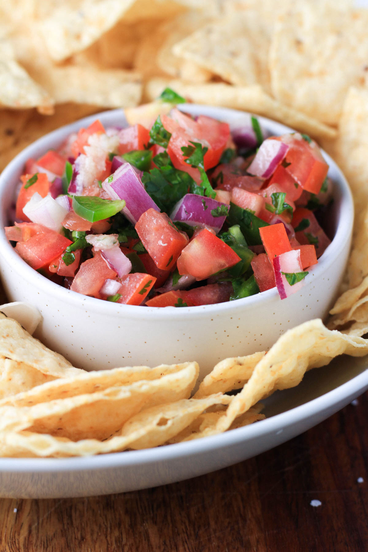 A white bowl, from the side filled with vegan pico de gallo in a white bowl with tortilla chips.
