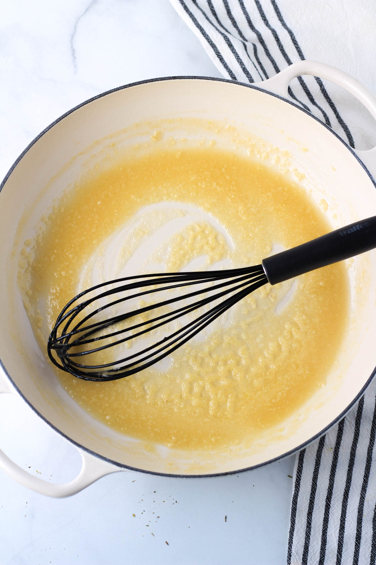 A large white skillet with a whisk and a roux.