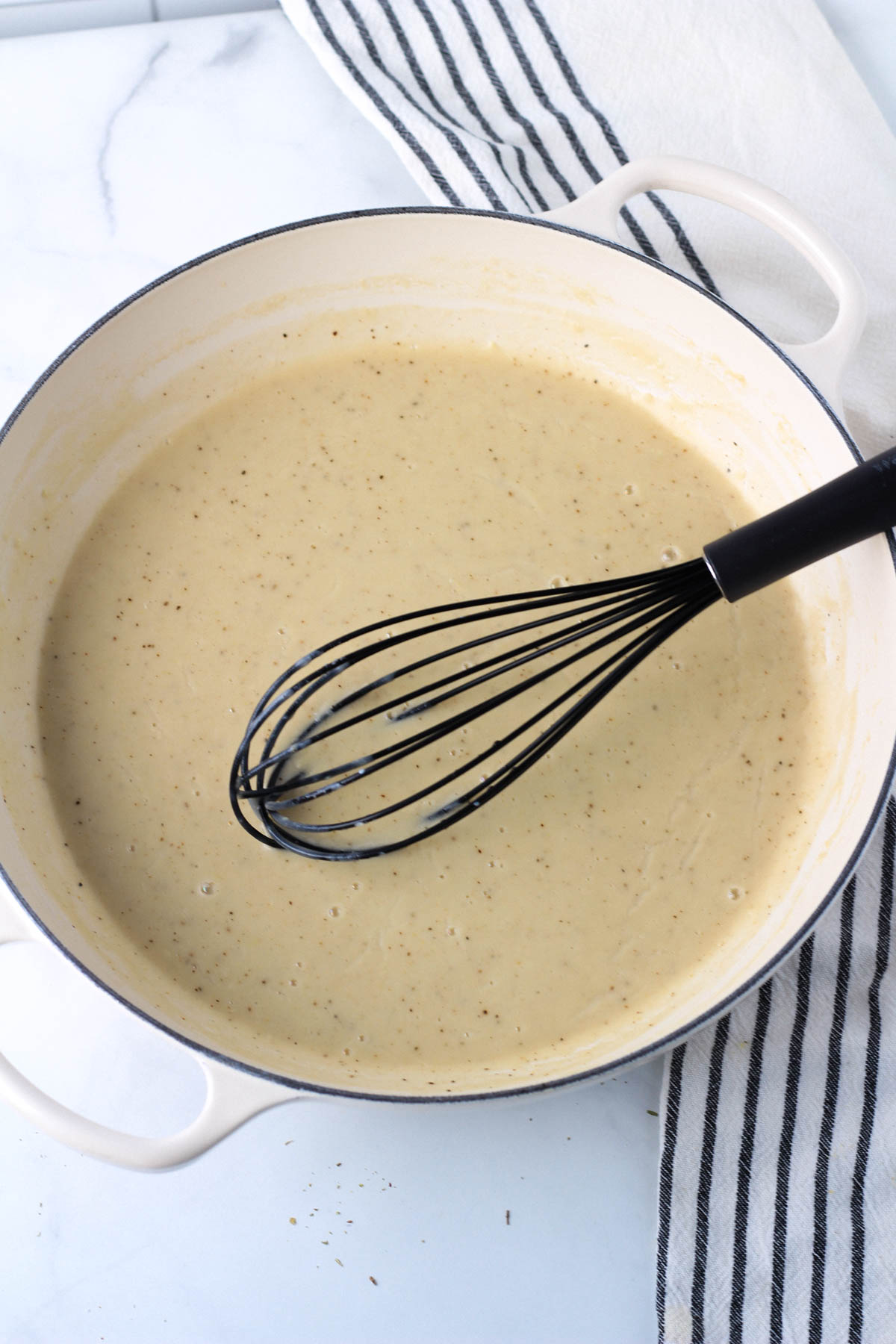 A large white skillet with garlic cream sauce after thickening.