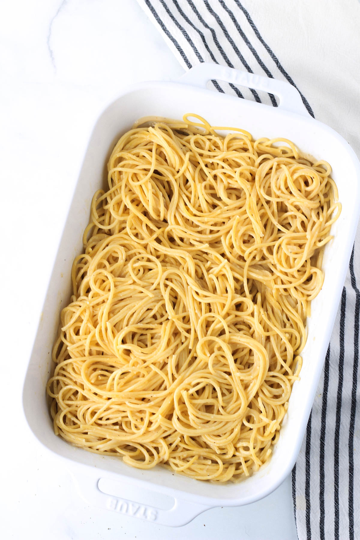 A large white baking dish with cooked spaghetti pasta coated in the garlic cream sauce.