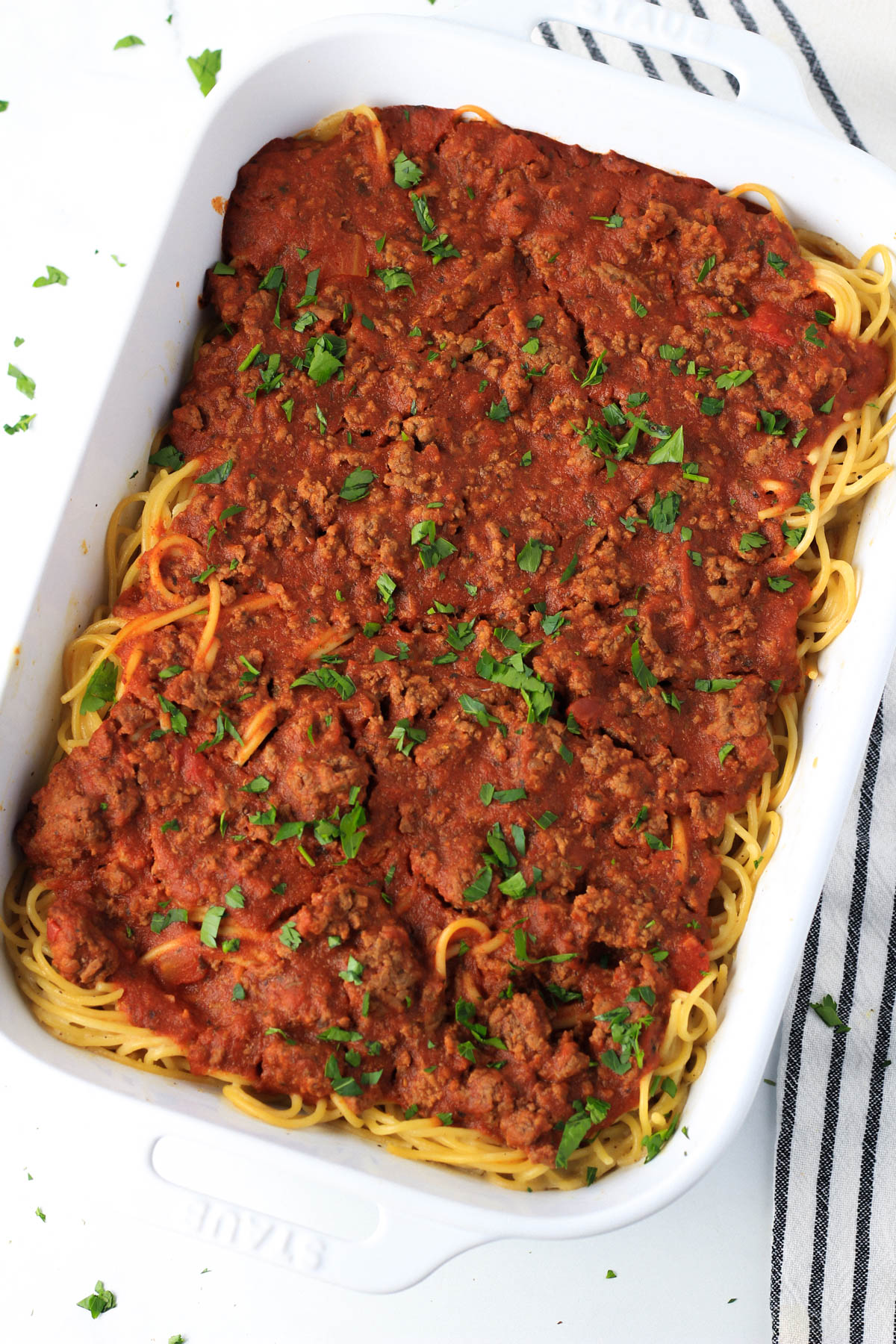 Red and white pasta in a white baking dish topped with fresh parsley after baking.