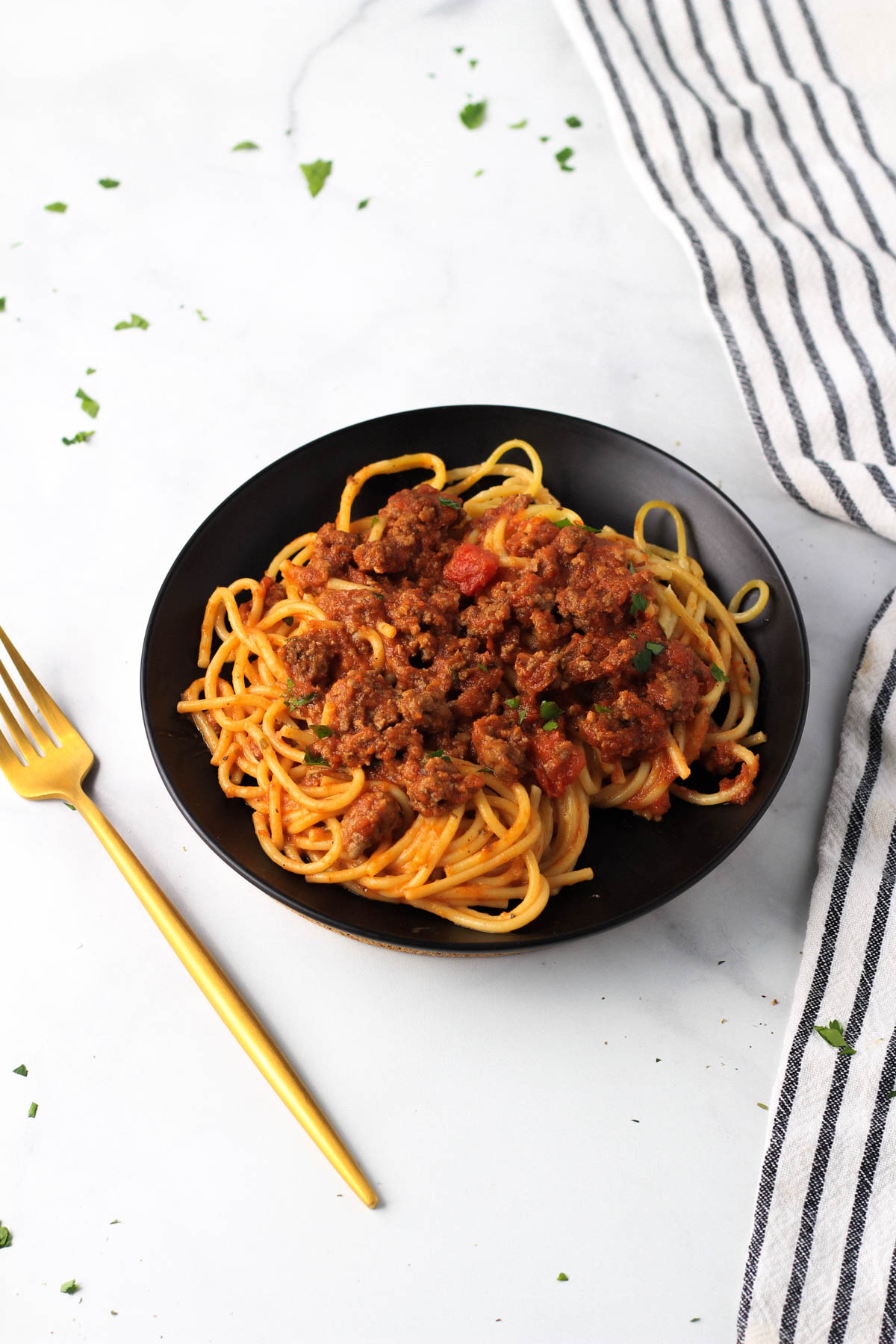 A small black plate with red and white pasta and a gold fork to the left of the plate.