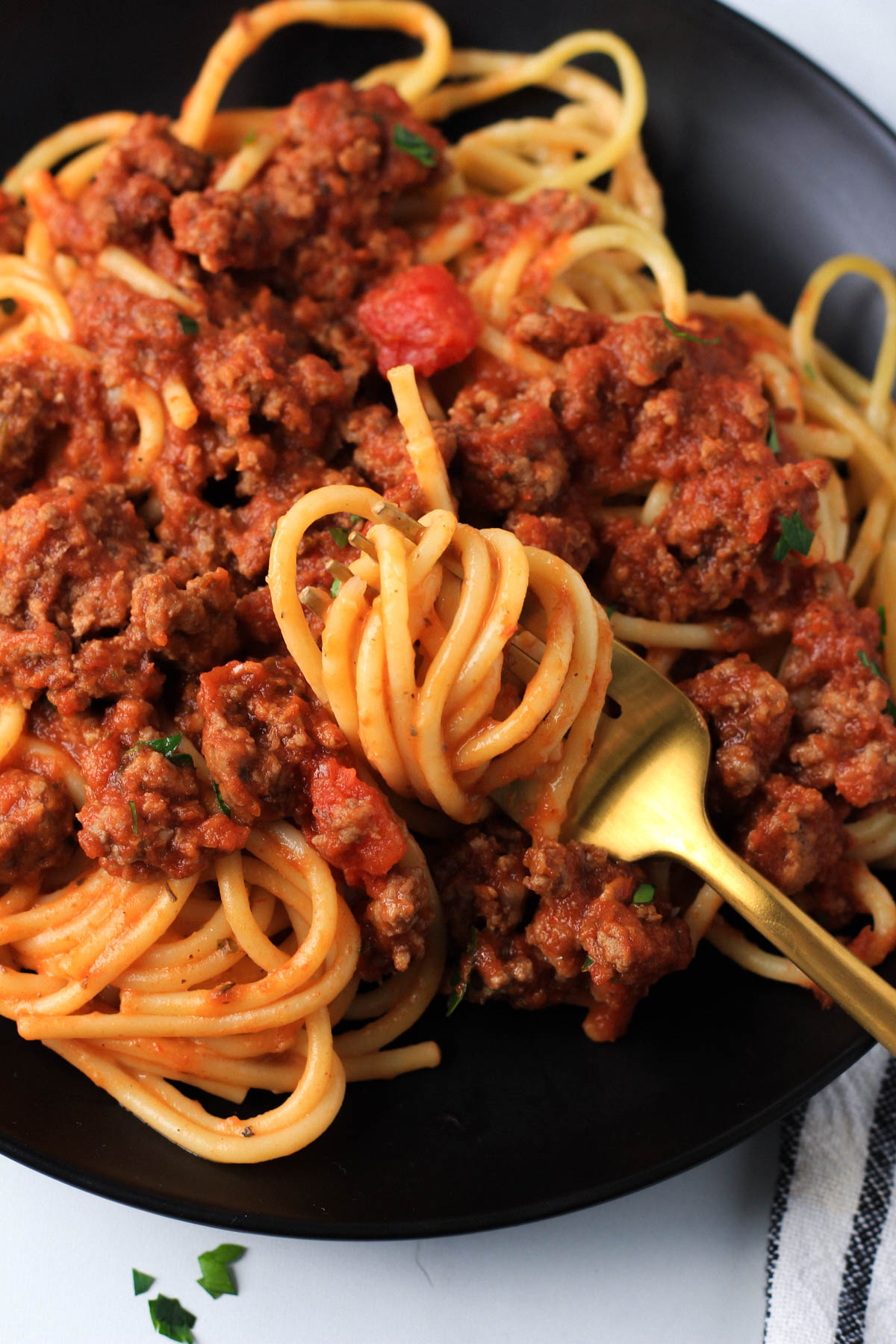 A gold fork with pasta twirled on the fork over a bed of red and white pasta on a black plate.