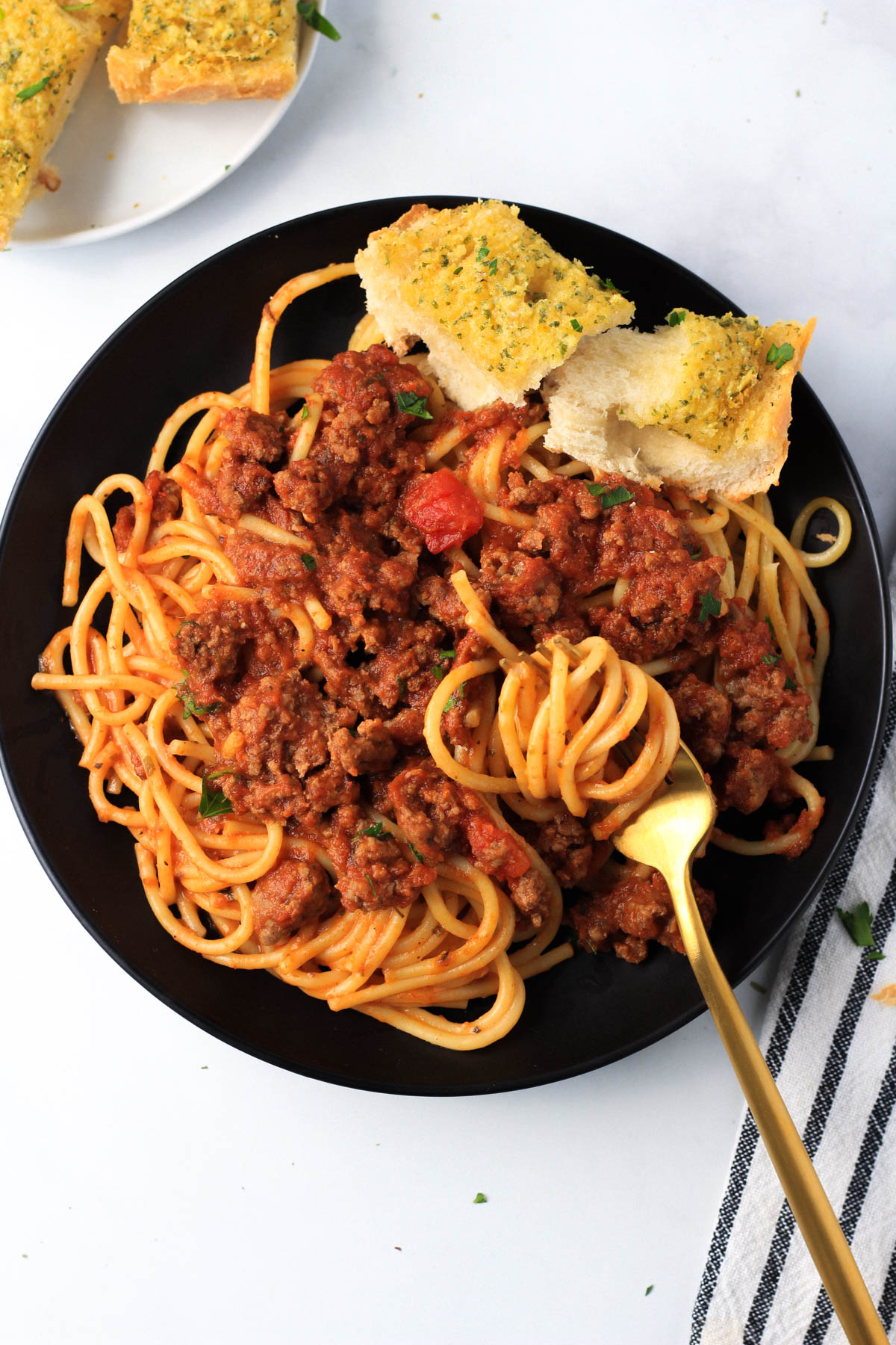 A small black plate with a serving of red and white pasta with a gold fork and a slice of vegan garlic bread on the plate.