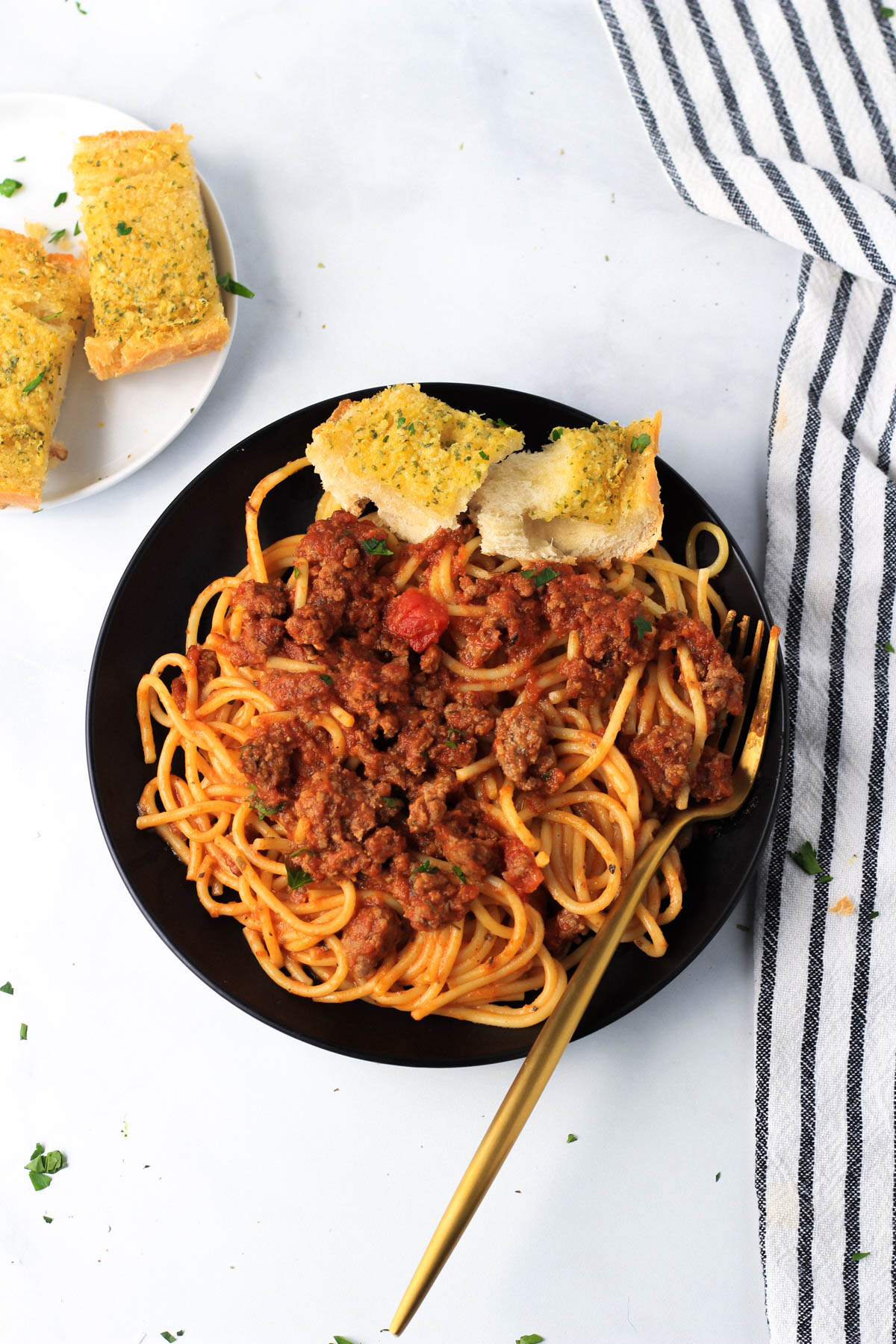 A small black plate with red and white pasta and garlic bread on a white counter with a small plate of garlic bread in the top left corner.