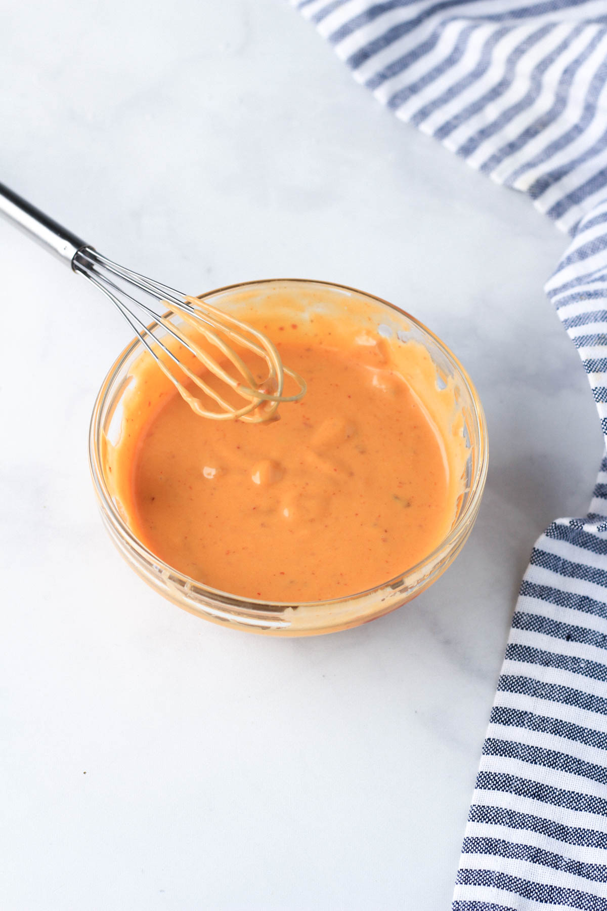 A small glass bowl with a small whisk and chipotle dressing mixed together.