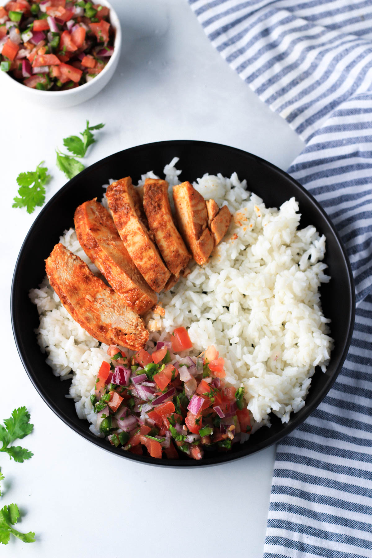 A black plate with rice, southwest chicken, and pico de gallo.