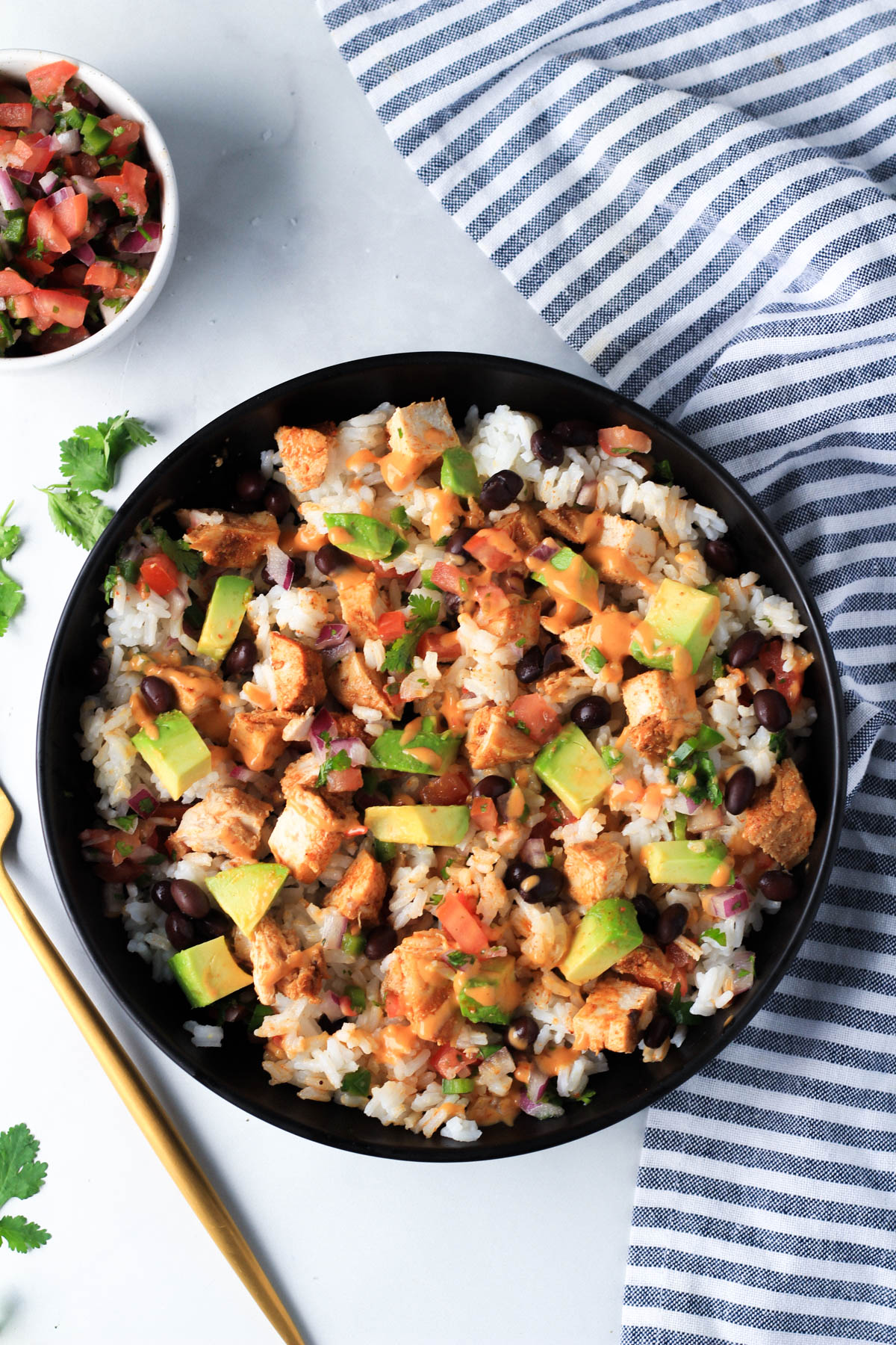 A southwest chicken burrito bowl with chipotle dressing and a gold fork to the left with a small bowl of pico de gallo in the top left.