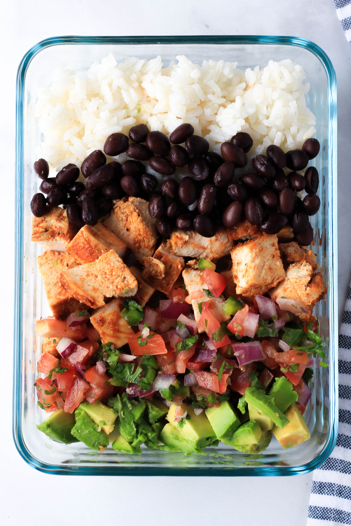 A glass storage container with a southwest chicken burrito bowl assembled to-go.