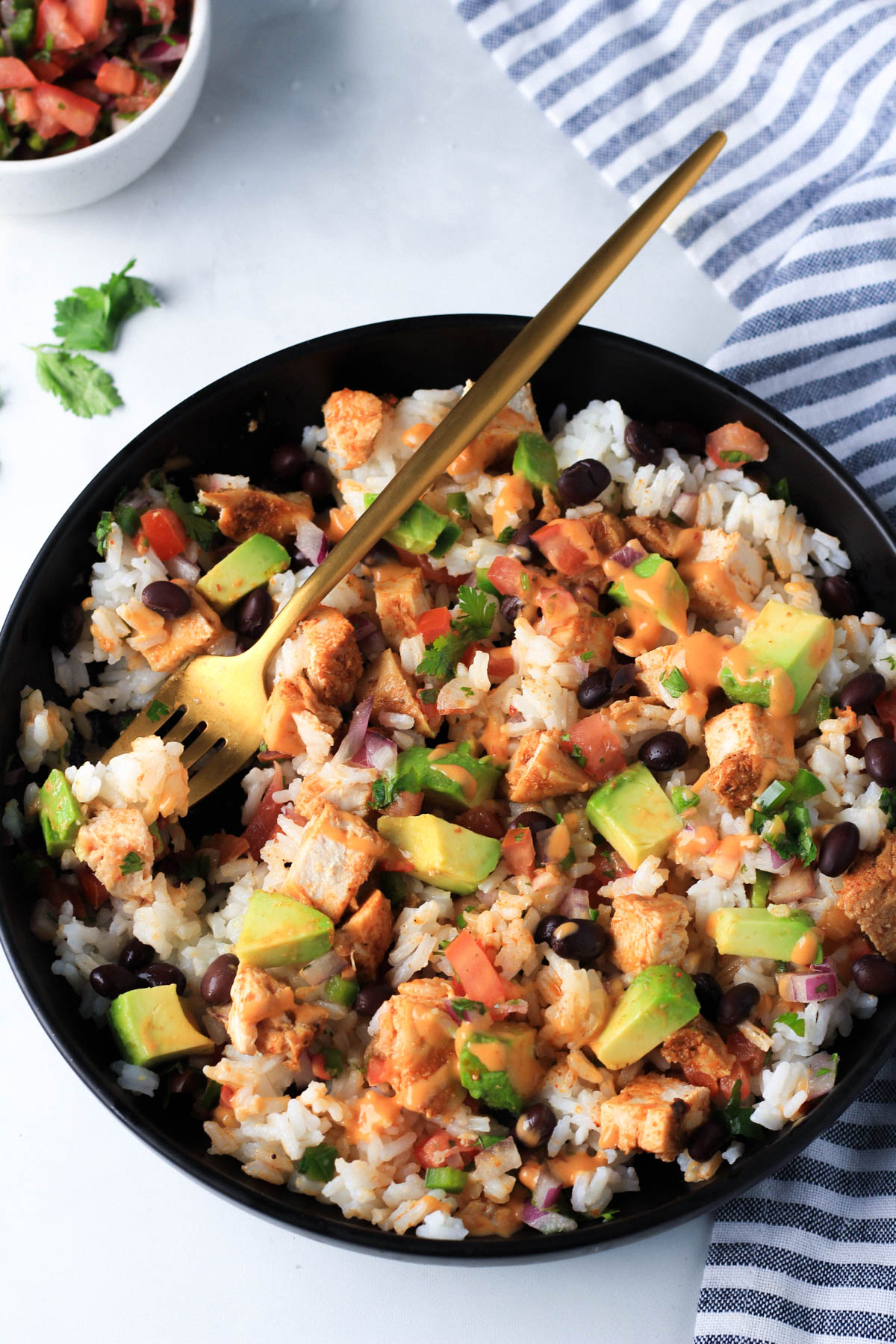 A black bowl with a tossed southwest chicken burrito bowl and a gold fork in the bowl with a bite on the fork.