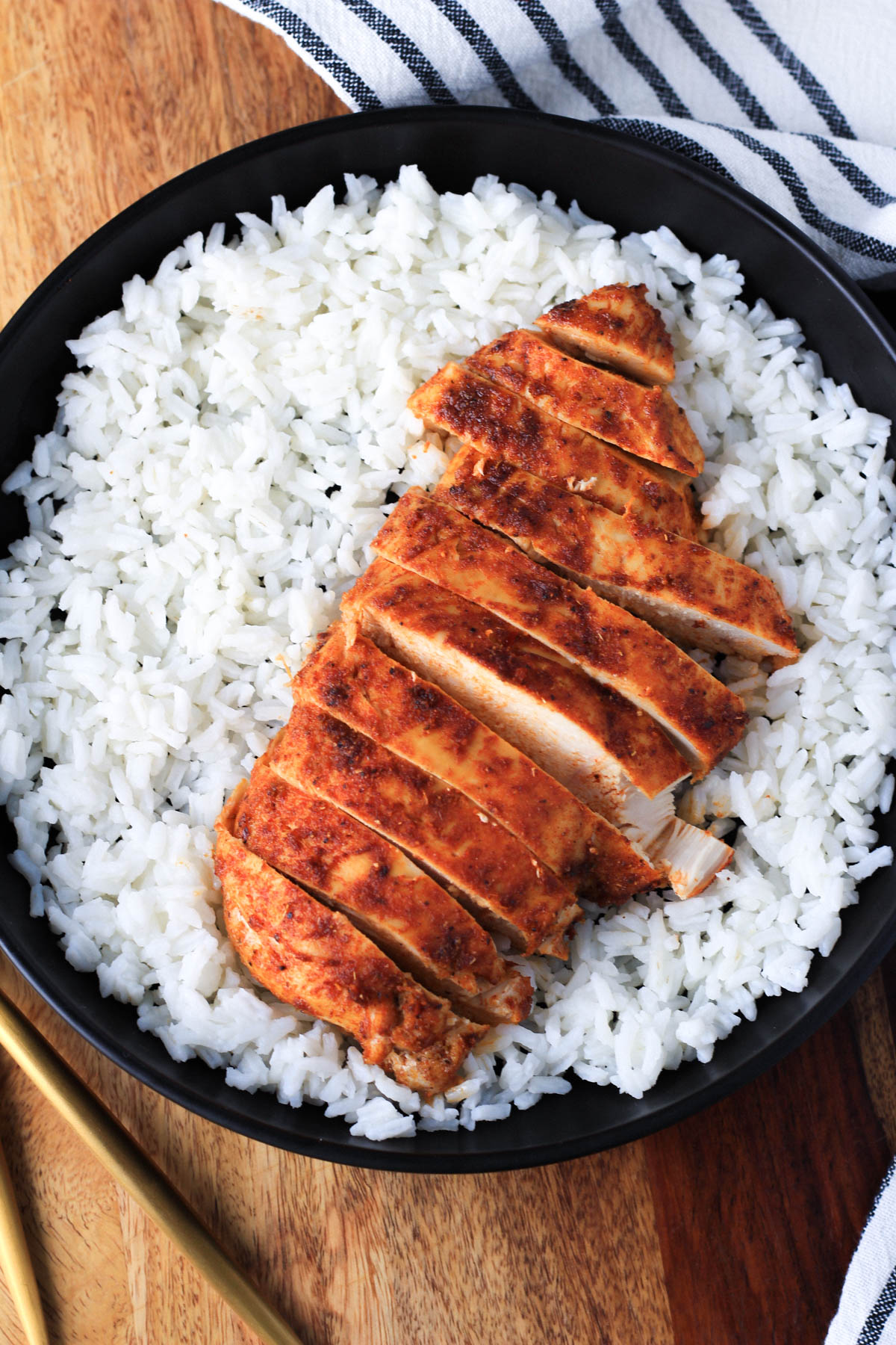 A black bowl with rice and a southwest chicken breast sliced on top.