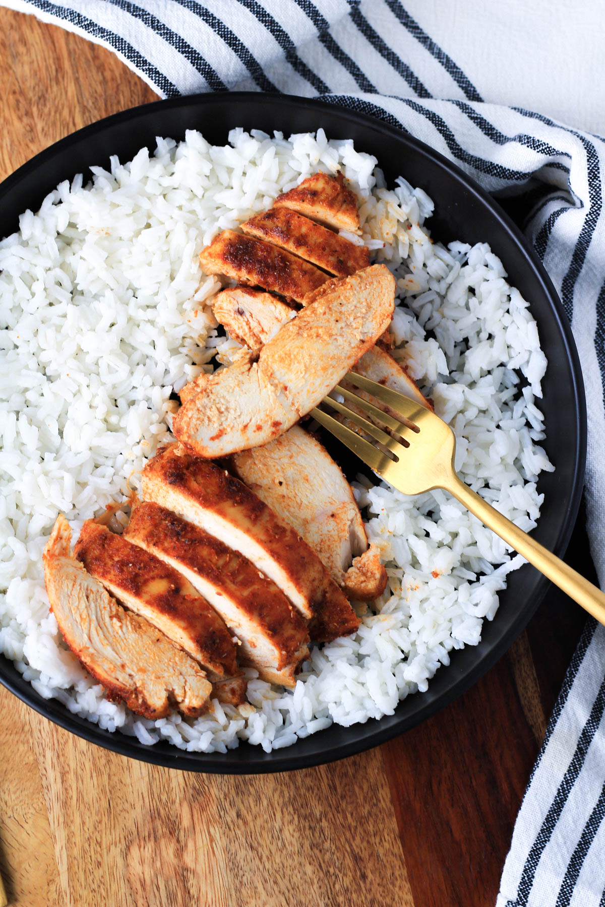 A gold fork with a slice of southwest chicken on a black plate with rice.