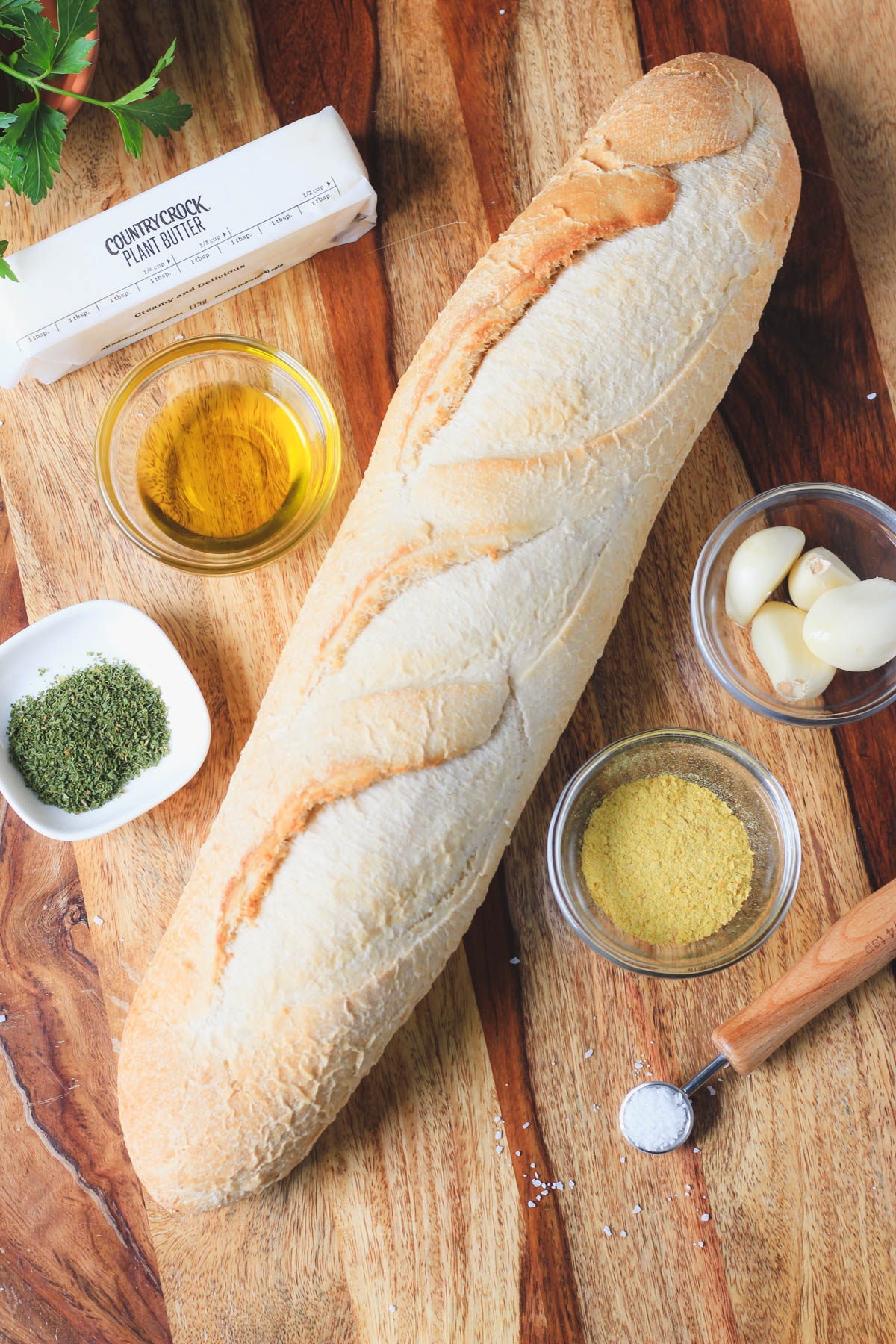 Ingredients for vegan garlic bread on a wooden counter.