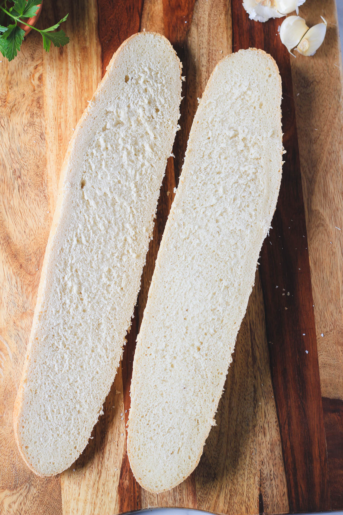A loaf of French bread cut in half lengthwise on a wooden counter.