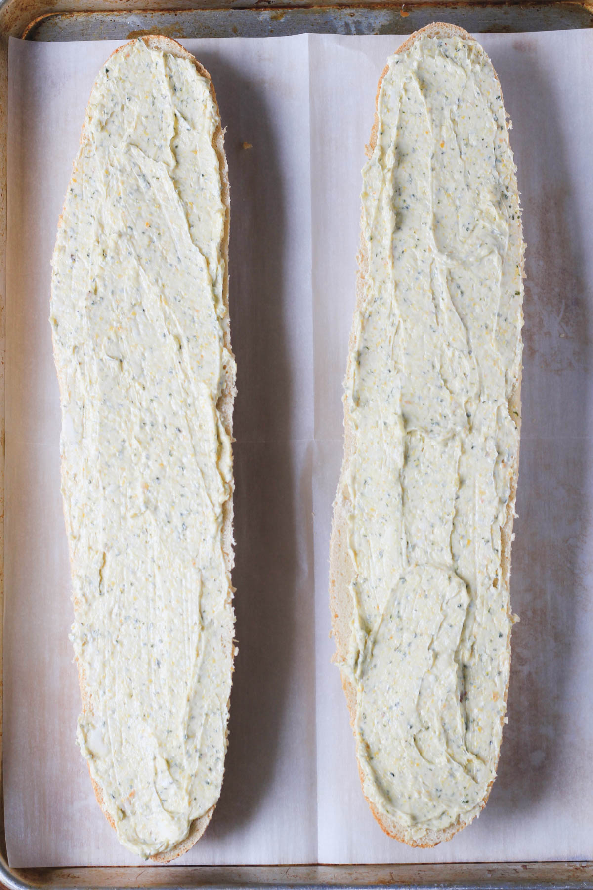 A parchment paper covered baking sheet with two unbaked halves of garlic bread.