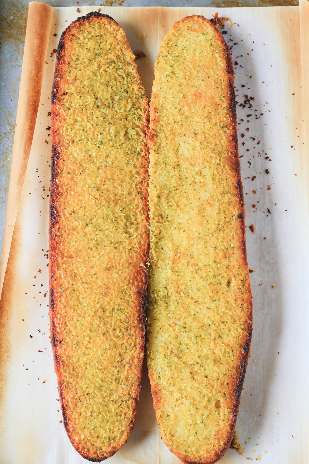 Two halves of oven-baked vegan garlic bread on a parchment paper lined baking sheet after baking.