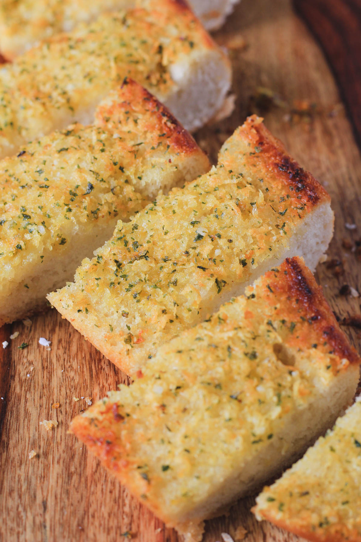 A wooden cutting board topped with slices of oven-baked vegan garlic bread.