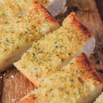 A close up of three slices of vegan garlic bread on a wooden cutting board.