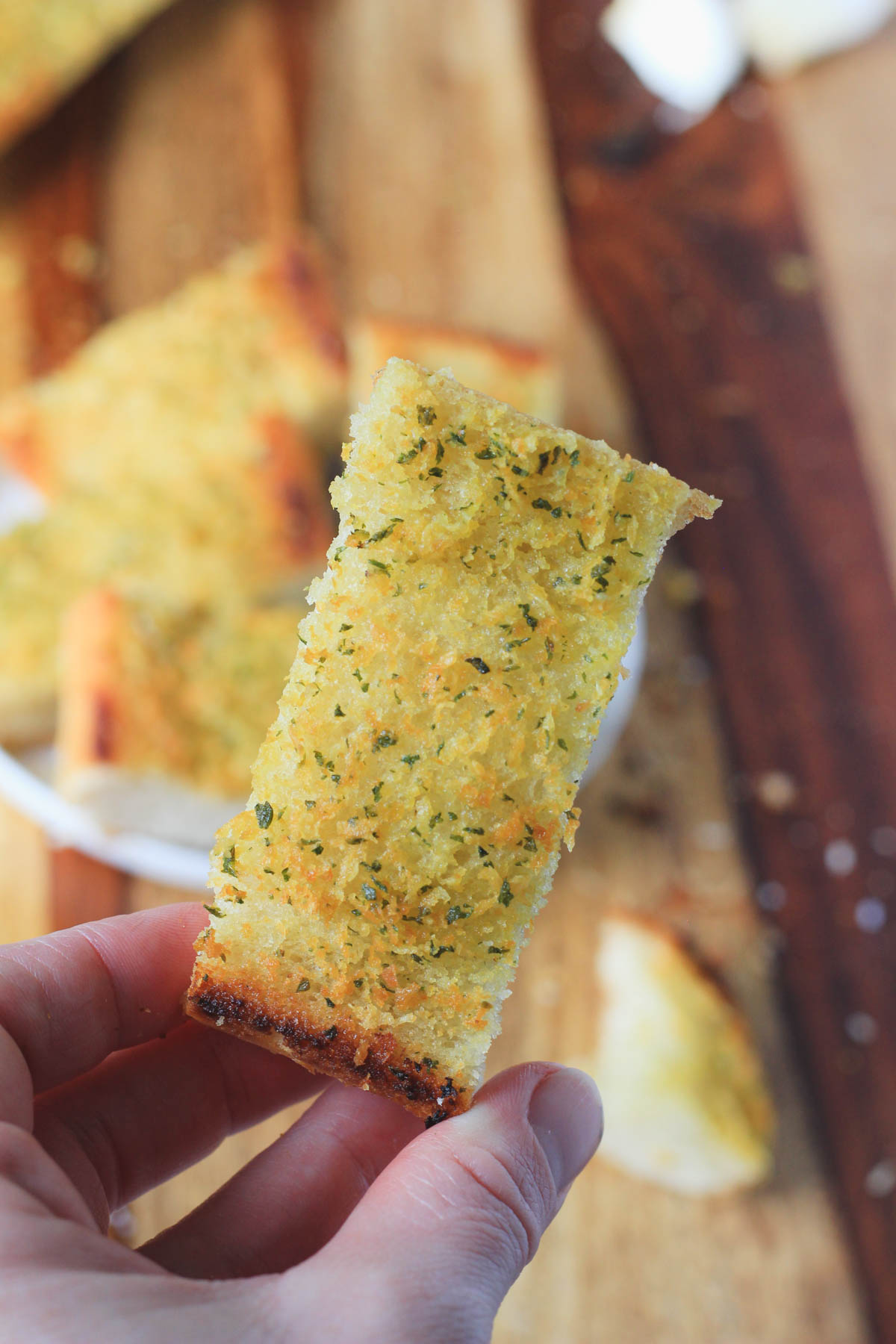 A hand holding a slice of vegan garlic bread.