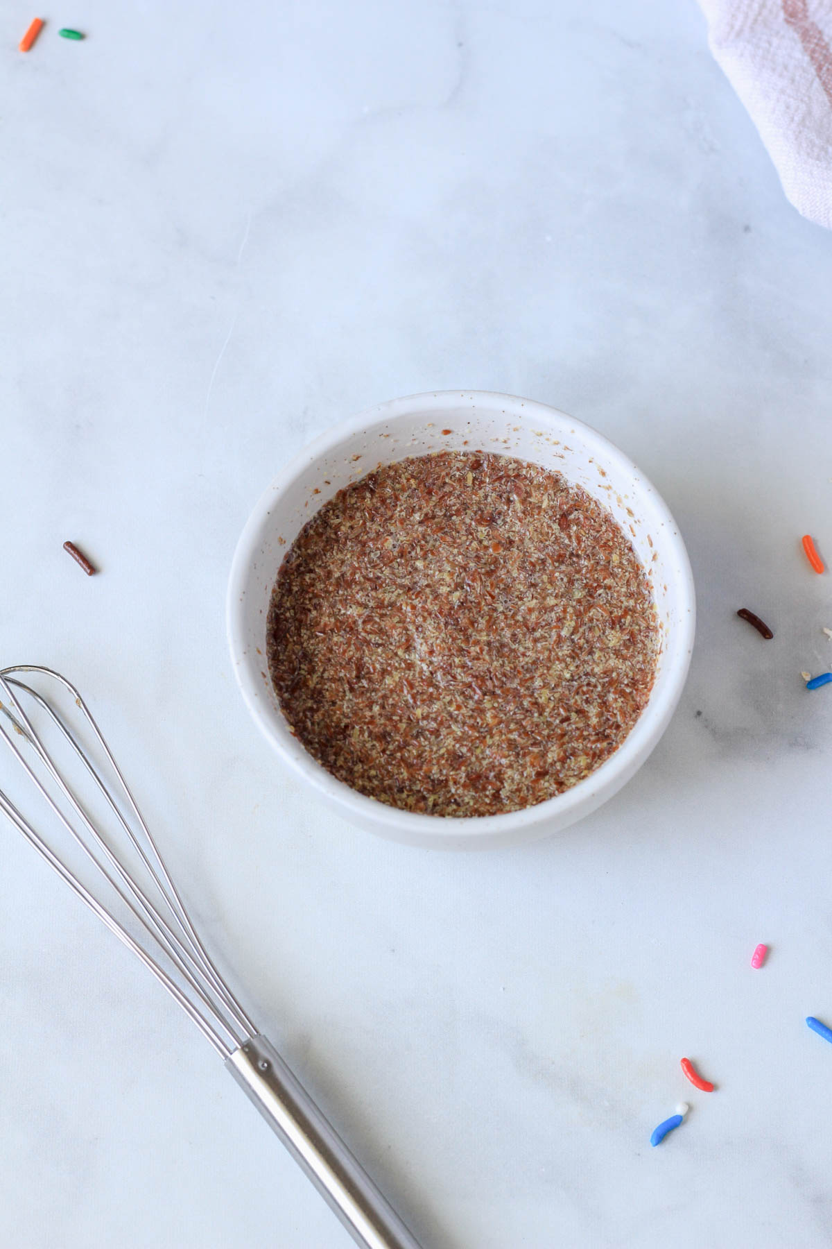 A small white bowl with a flax egg mixed together and a small whisk to the bottom left.