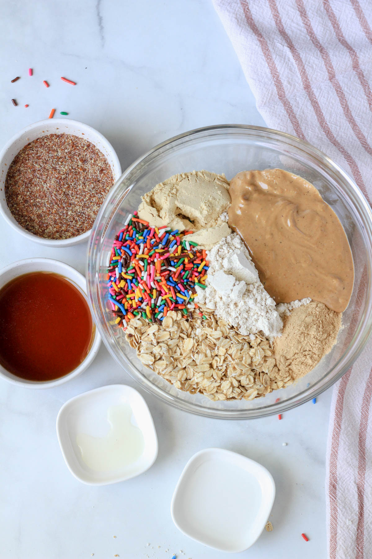 A large glass bowl with most of the ingredients for cake batter lactation bites poured in the bowl and the remaining ingredients to the left of the bowl.