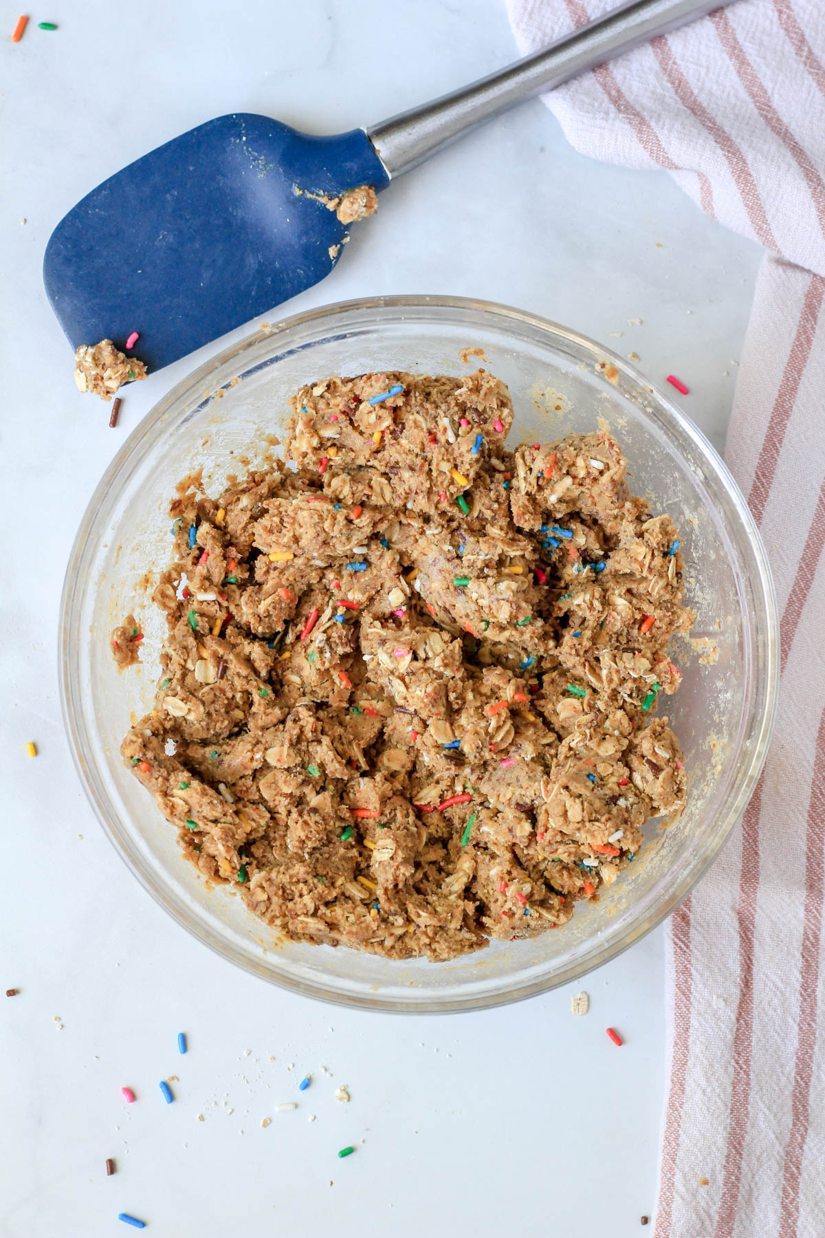 A glass bowl with cake batter lactation bites mixed together and a blue spatula above the bowl.