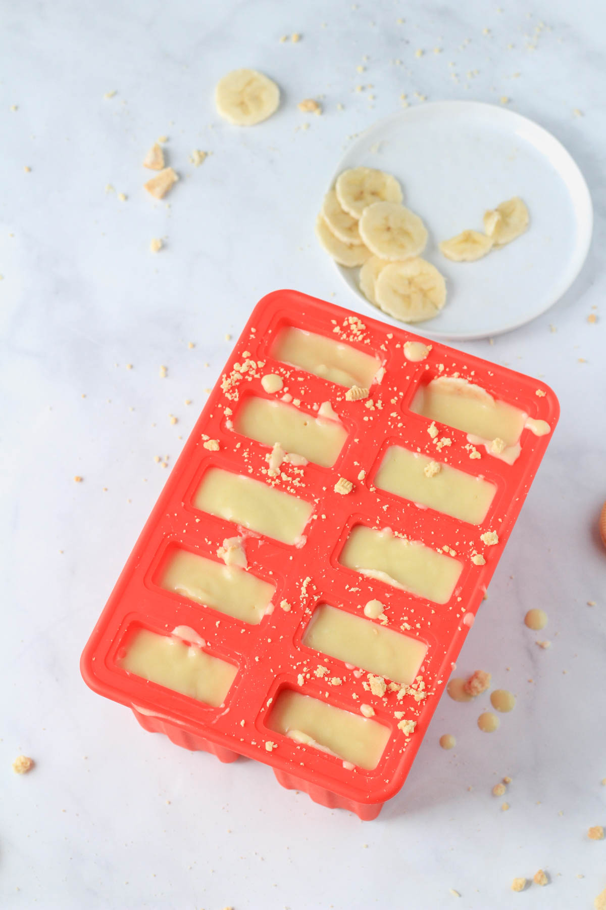A red popsicle mold filled with layers of crushed oreo, banana pudding filling, and banana.