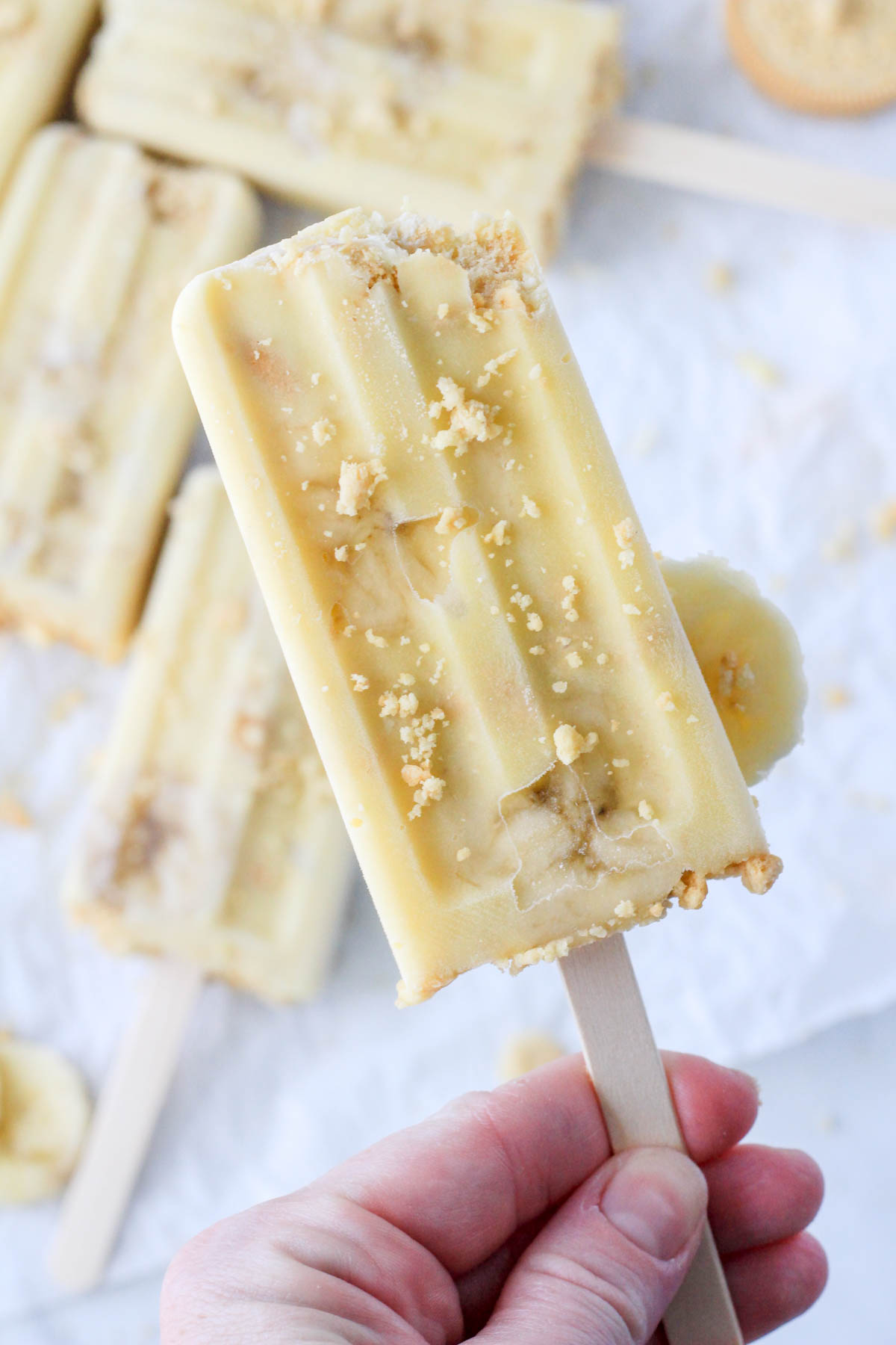 A hand holding a frozen banana pudding popsicle.