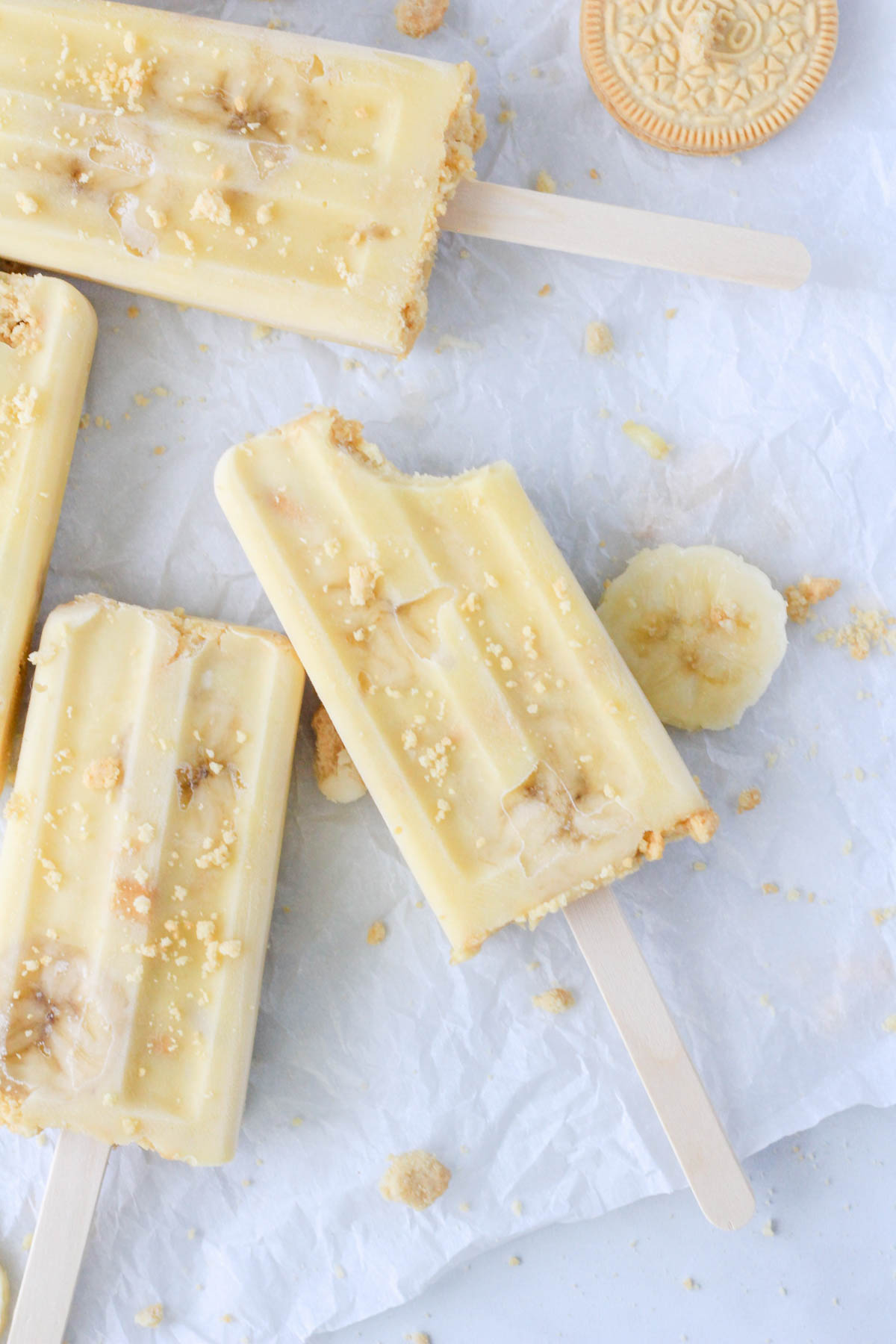 A bite taken out of a dairy-free banana pudding popsicle on a piece of parchment paper with three other banana pudding popsicles around.