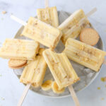 A white bowl filled with ice and topped with seven dairy-free banana pudding popsicles.