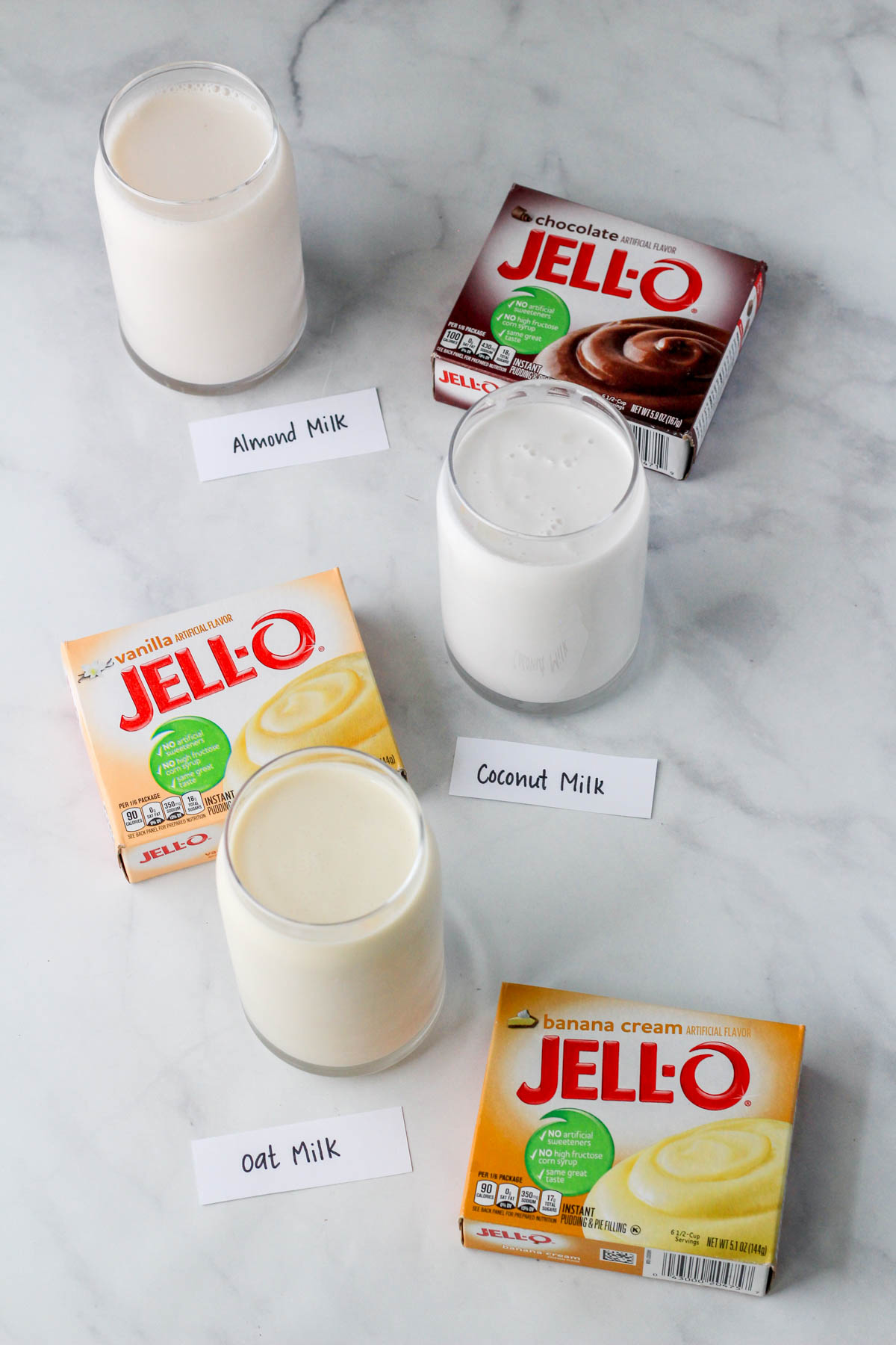 Three different dairy-free milks with three different boxes of jell-o pudding mix on a white counter.