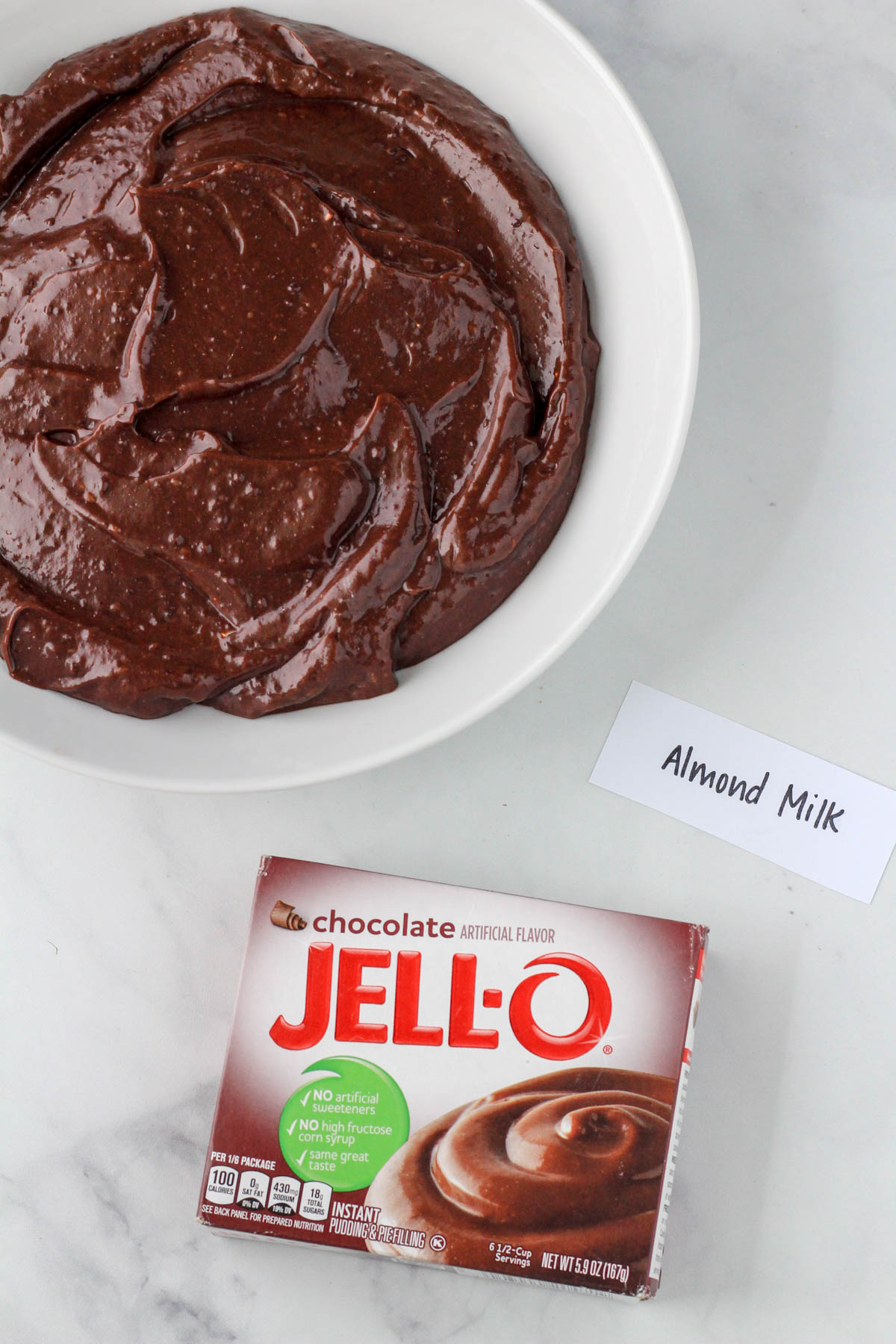 A white bowl of chocolate jell-o pudding with almond milk.