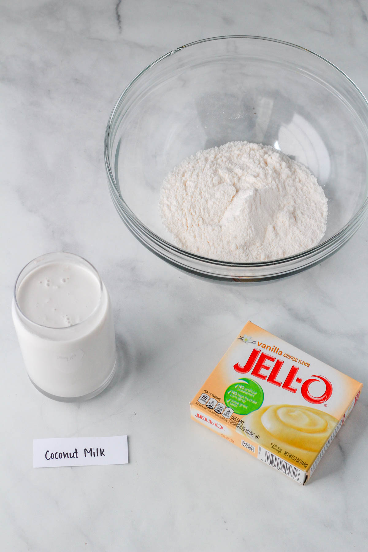 A glass bowl with vanilla instant jell-o pudding and a glass of coconut milk below with the instant pudding box in the bottom right.