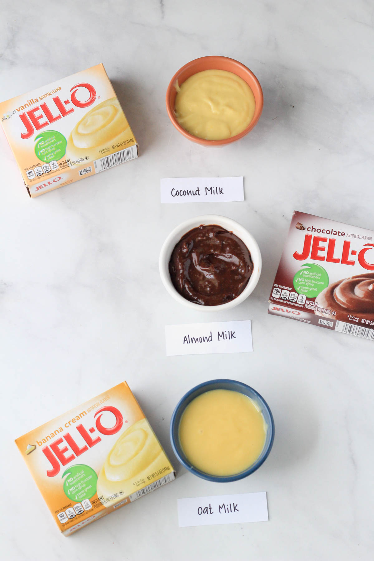 Three bowls with small servings of jell-o pudding made with three different types of dairy-free milk.