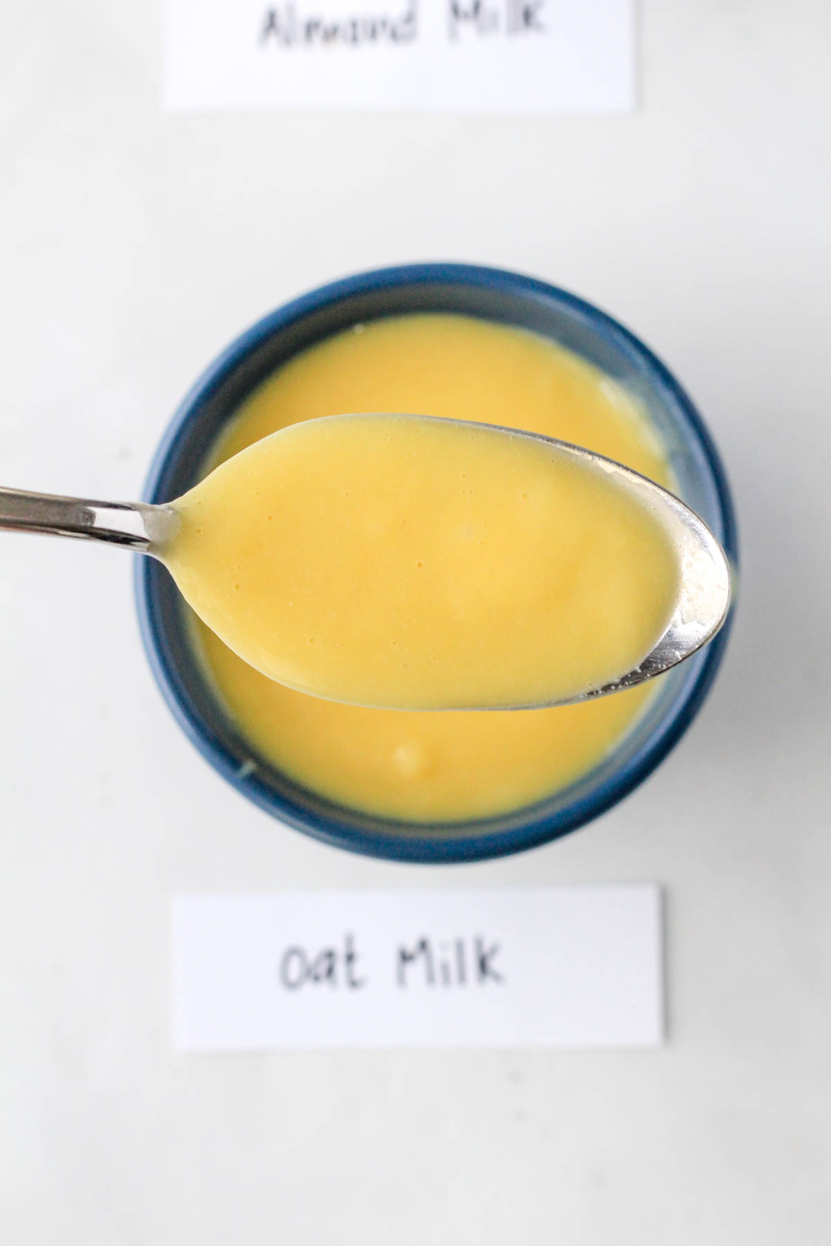 A blue bowl with banana pudding jell-o made with oat milk and a spoon of the pudding above.