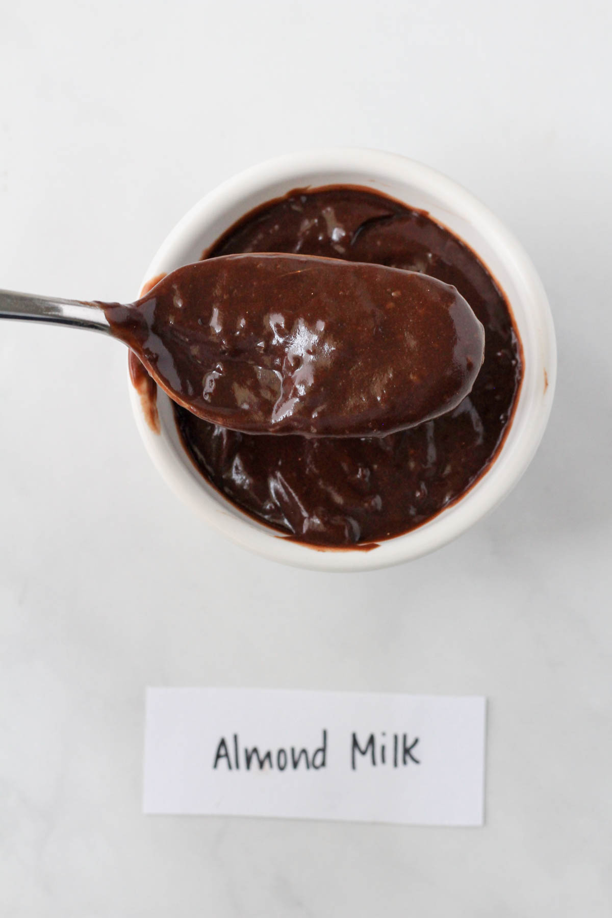 A white bowl with chocolate instant pudding and a spoon holding a scoop of the pudding made with almond milk.