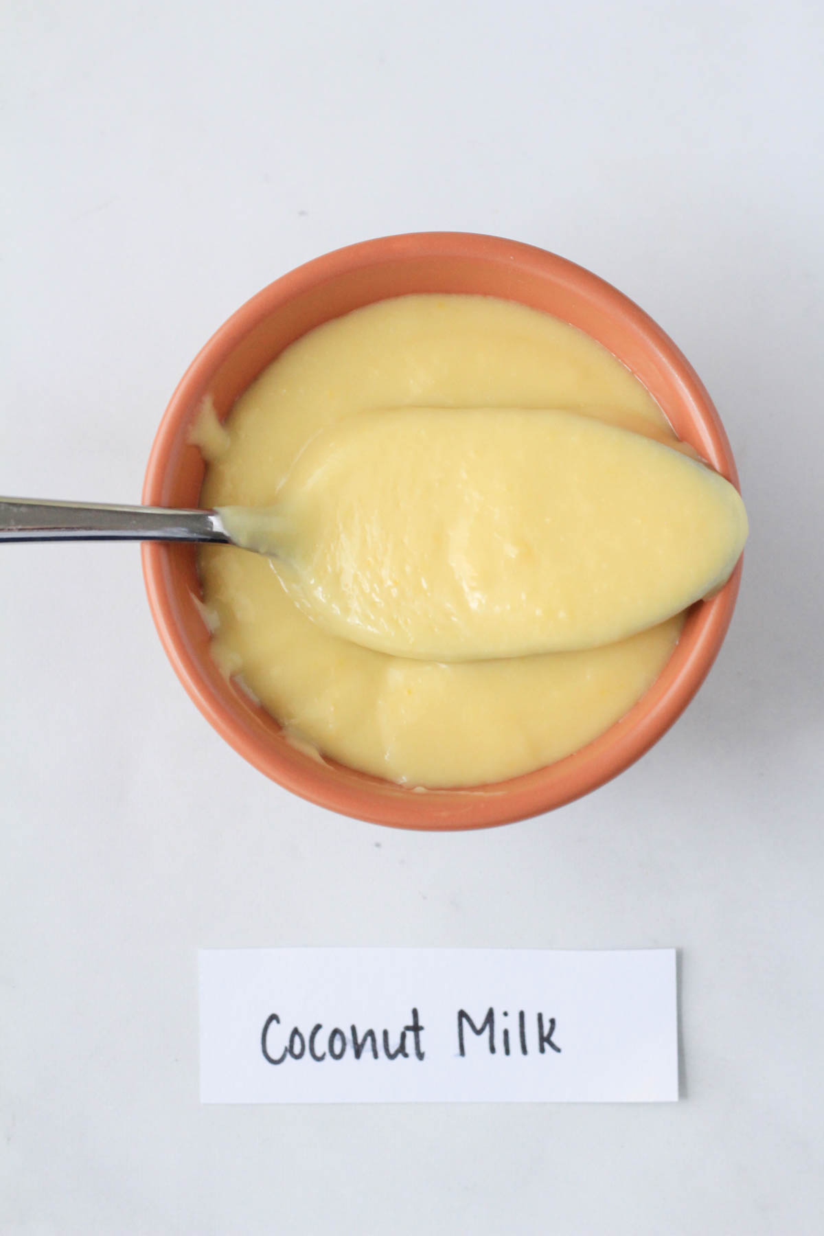 An orange bowl with vanilla instant pudding made with coconut milk and the word coconut milk at the bottom.