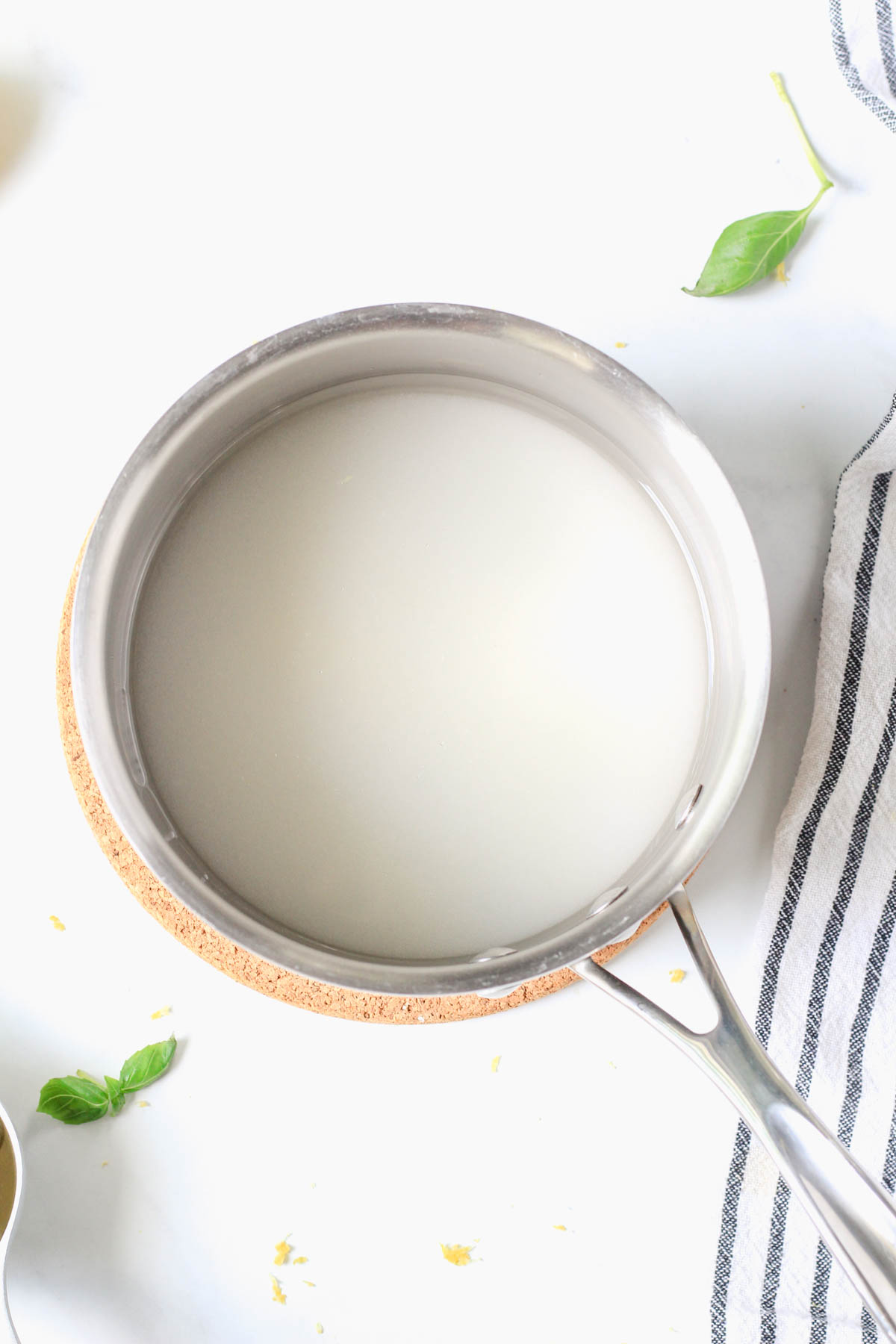 A silver sauce pan with water and sugar on a white counter.