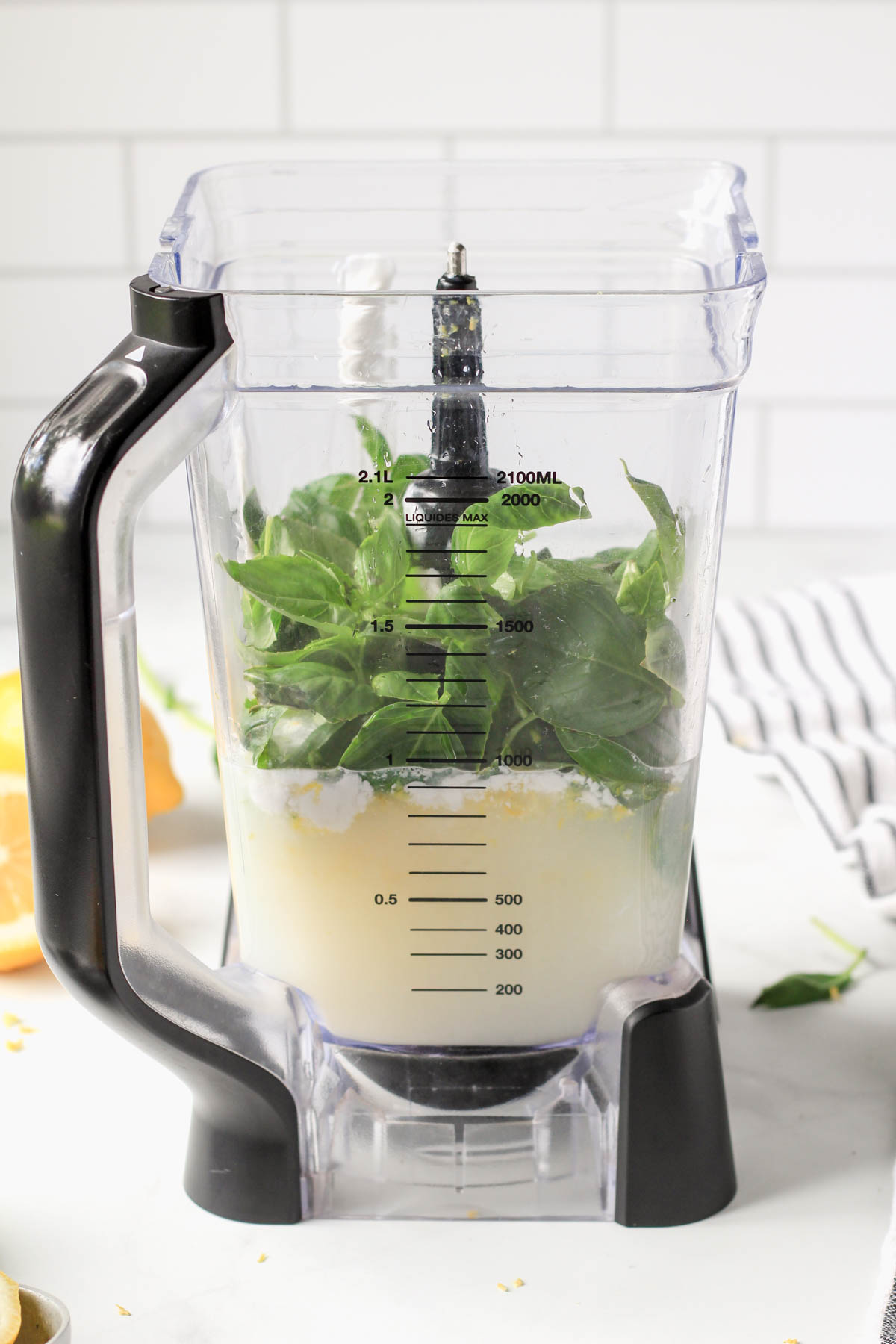 A blender pitcher with the ingredients for lemon basil popsicles before blending.