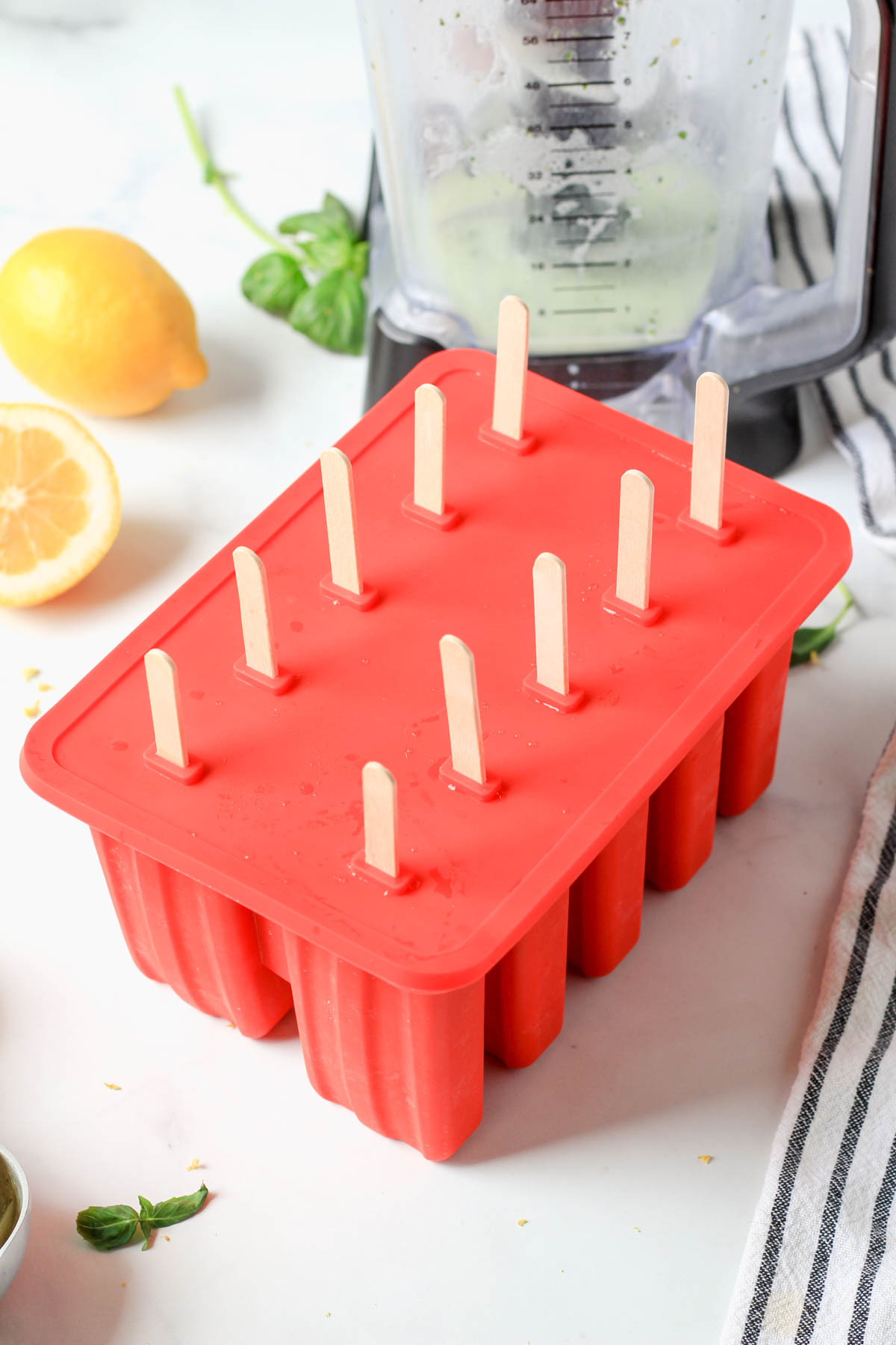 A red popsicle mold with wooden popsicle sticks poking out the top.
