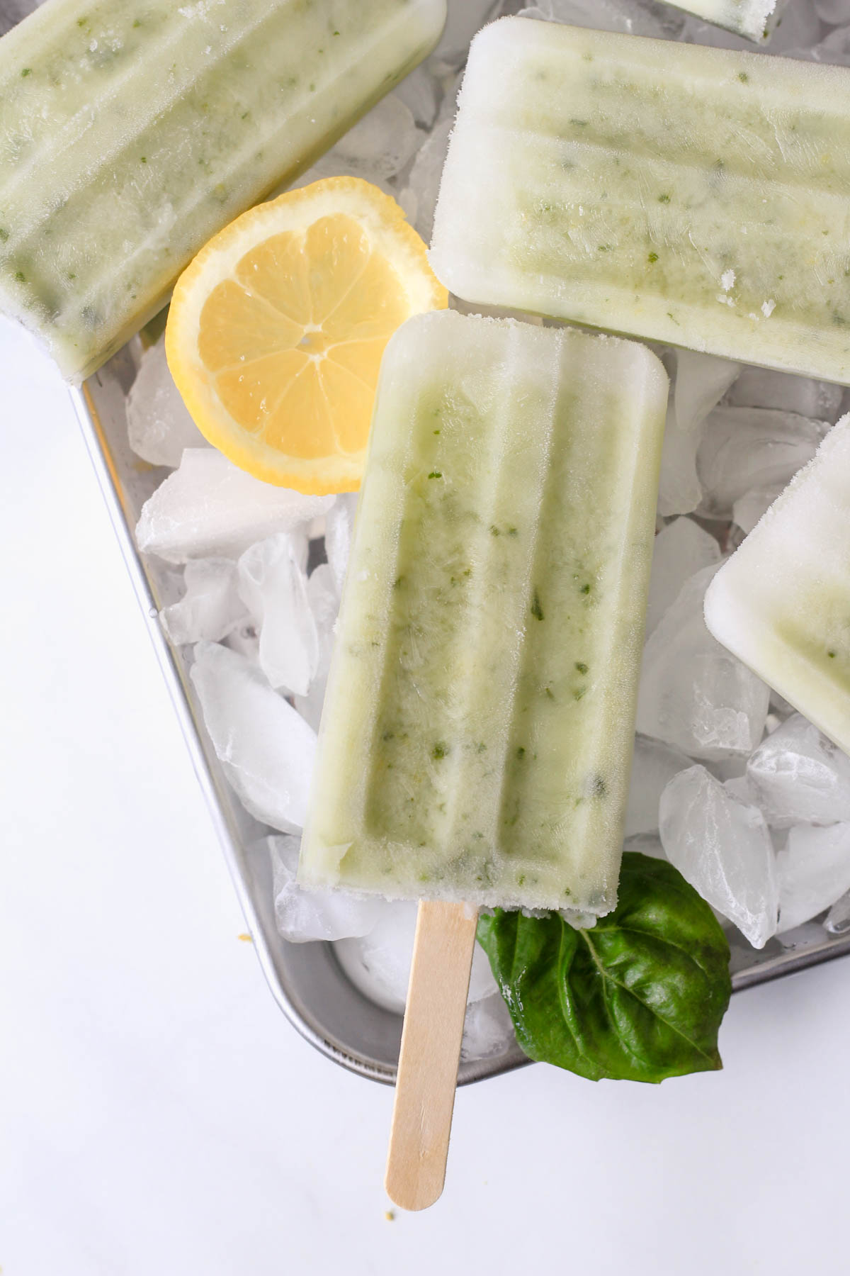 A lemon basil popsicle on a silver cookie sheet topped with ice.