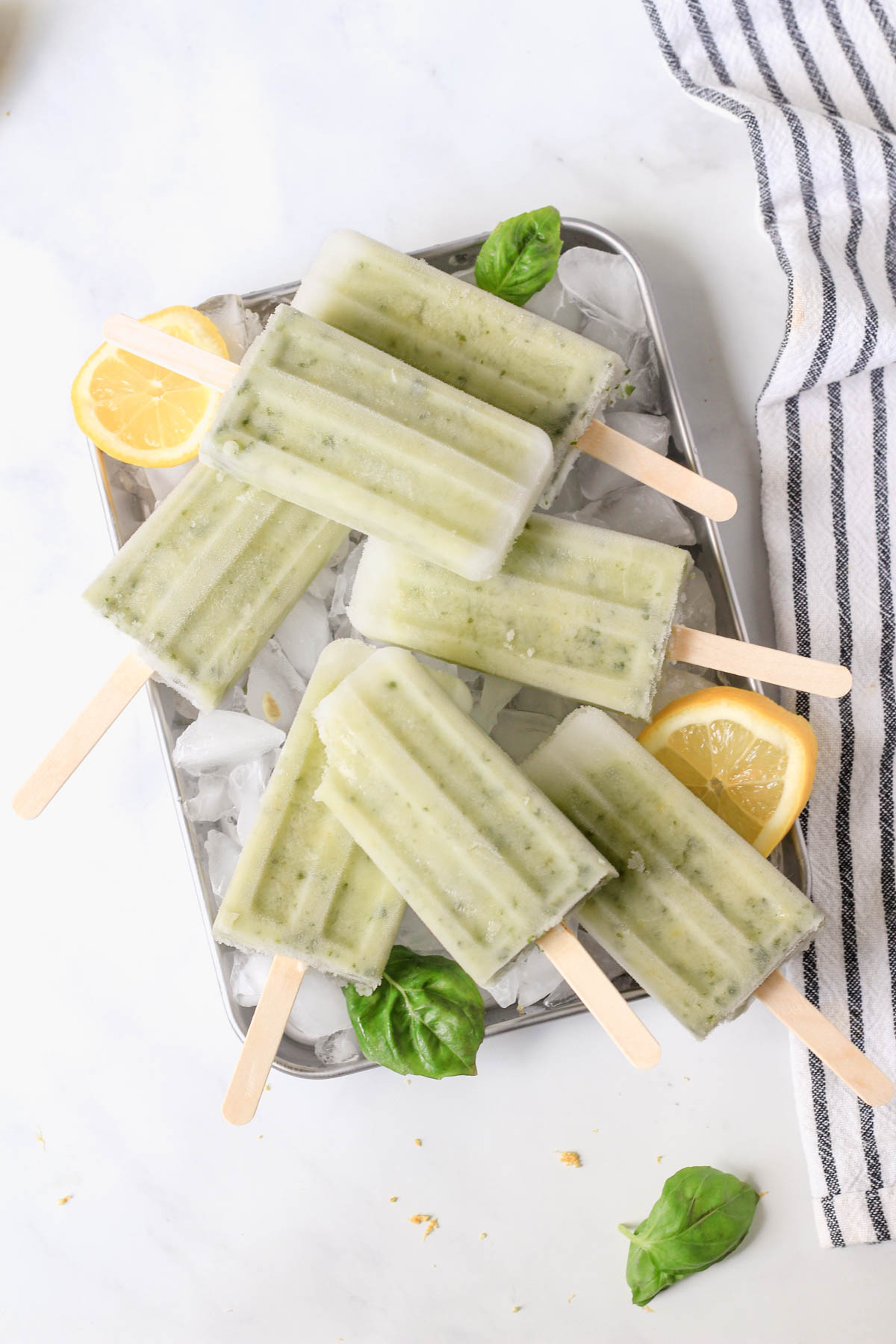 A white counter with a silver tray of lemon basil popsicles and ice.