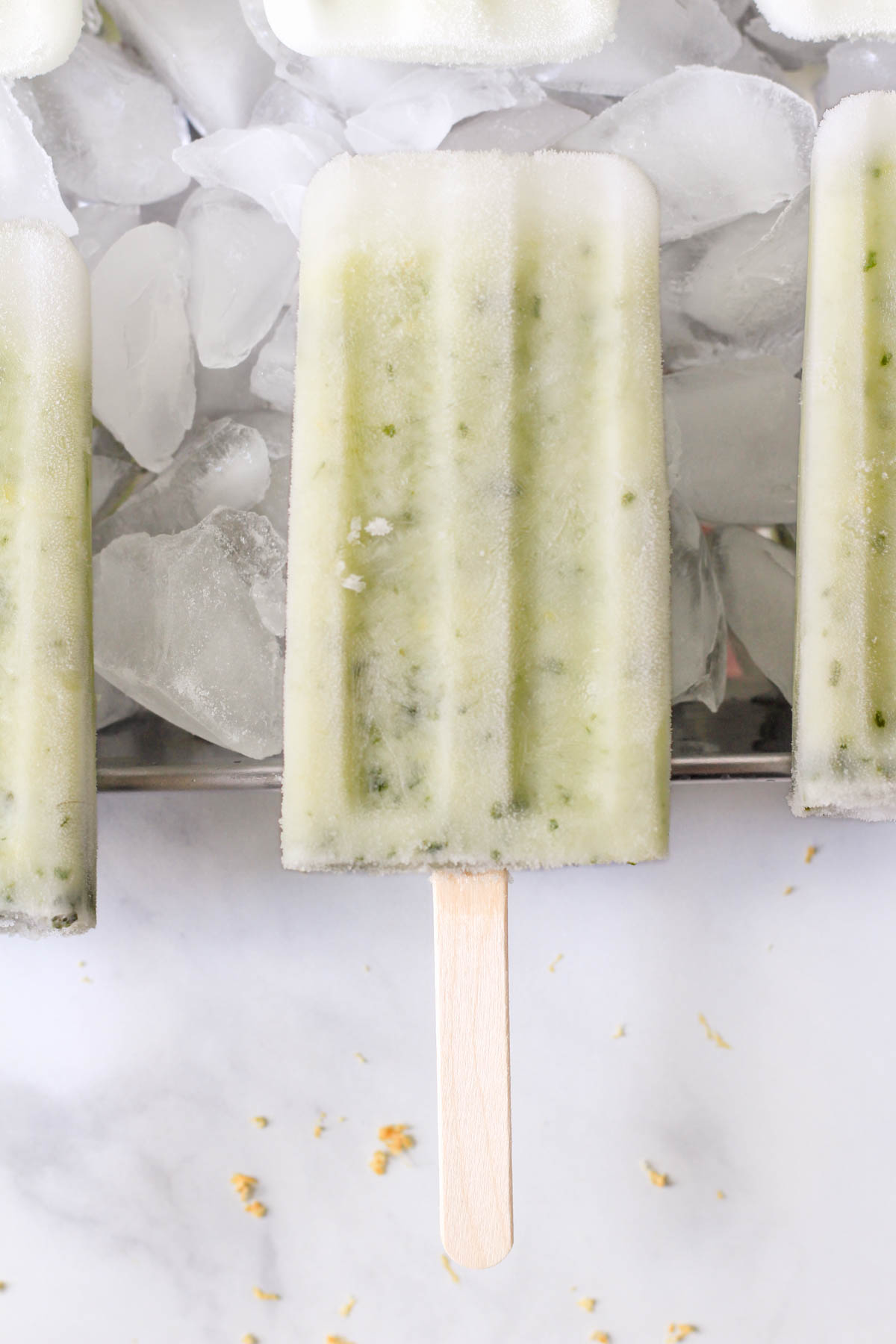 A lemon basil popsicle on top of ice in a silver pan.